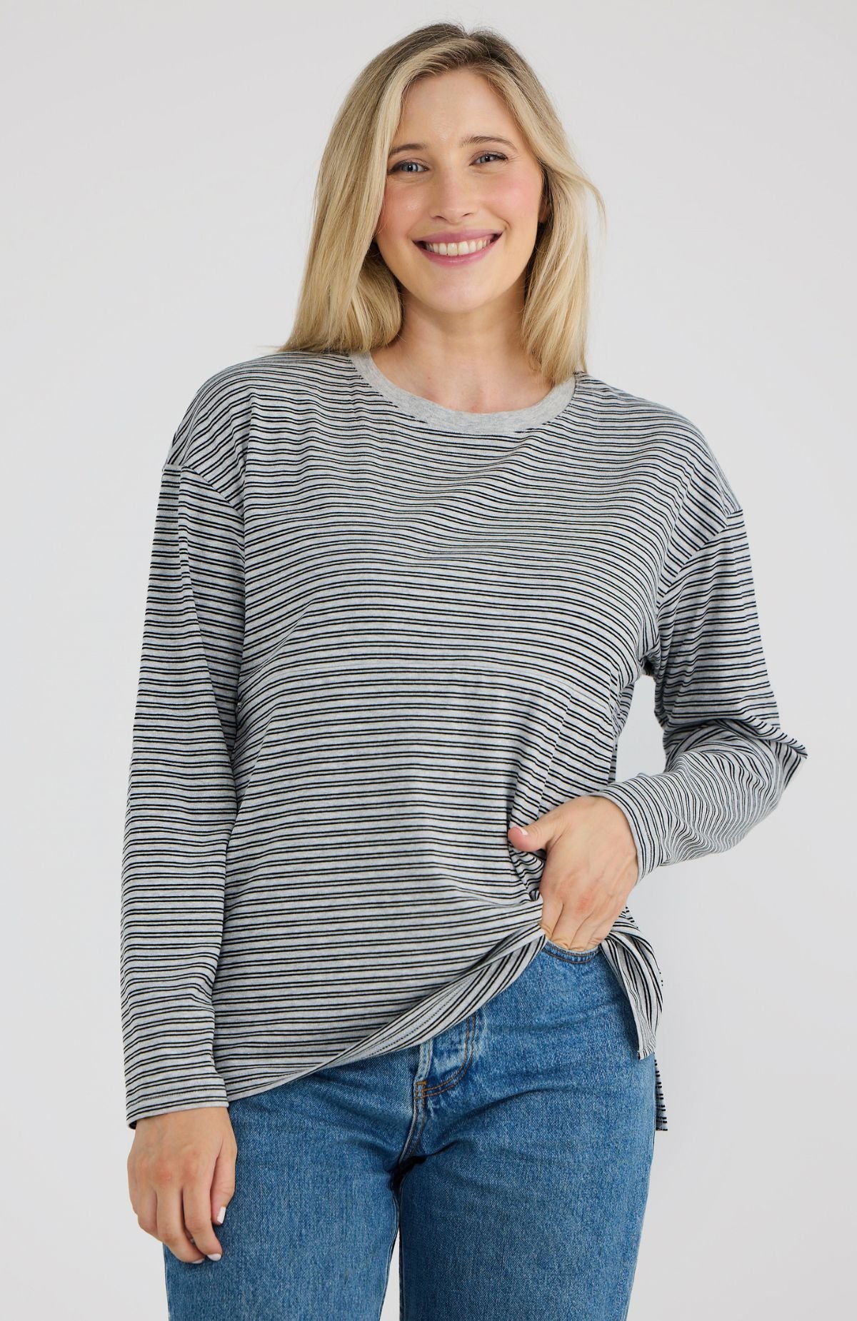 Woman wearing a striped long-sleeve top and blue jeans on a plain background