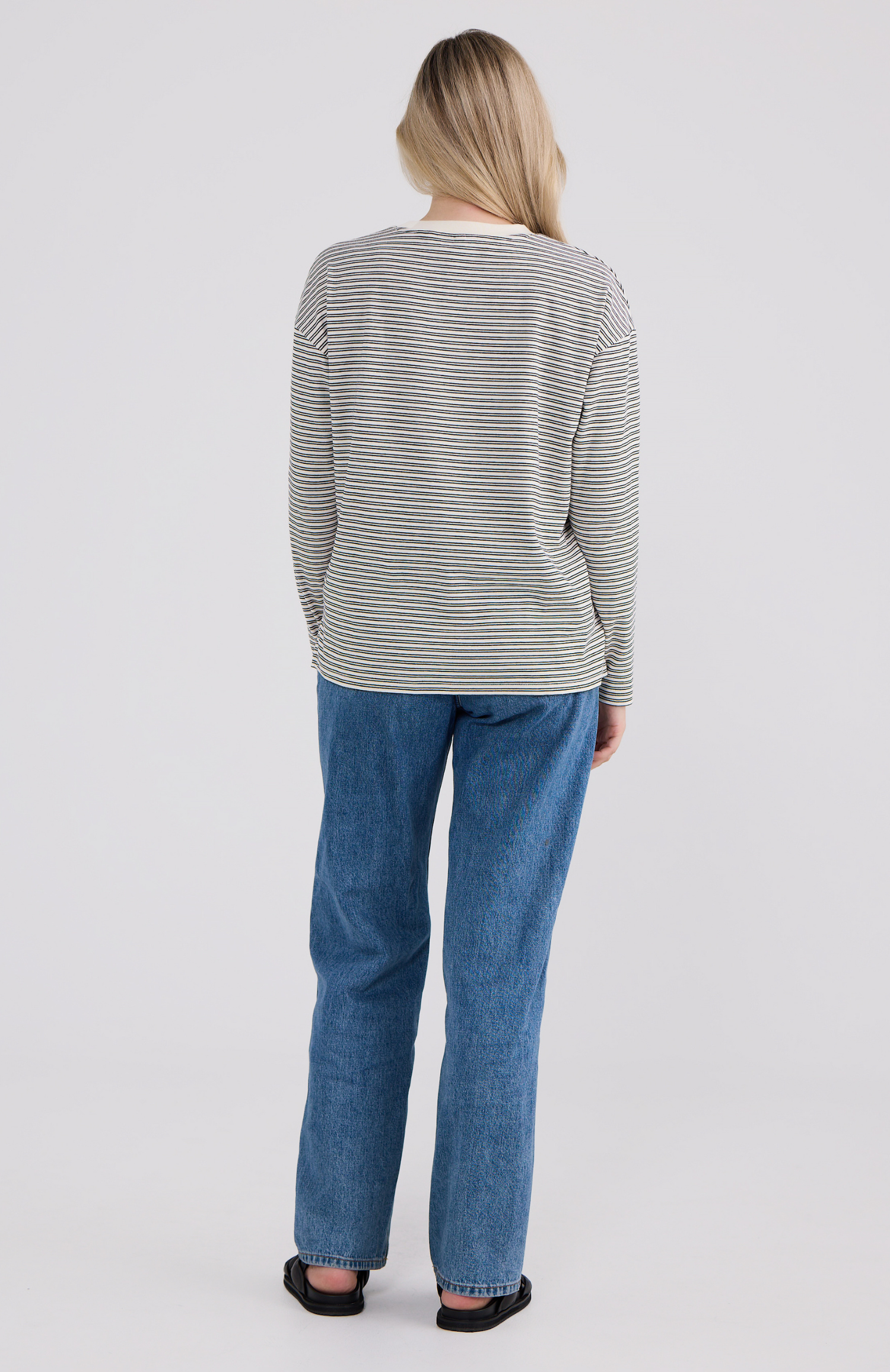 Person wearing a striped sweater and blue jeans on a white background