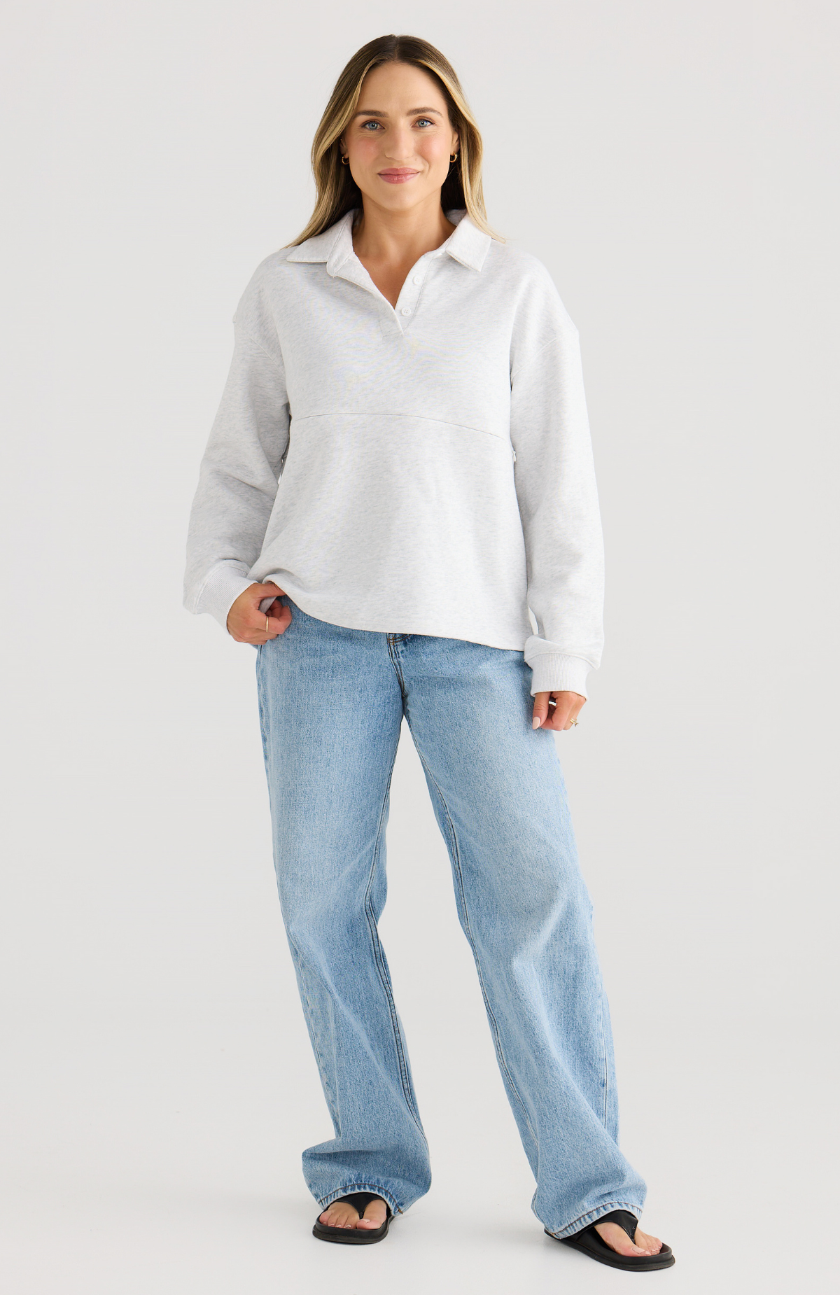 Woman wearing a grey polo jumper and blue jeans on a plain background