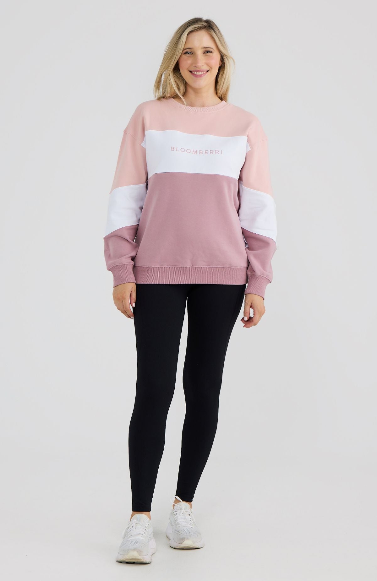 Woman wearing a pink and white color-blocked sweatshirt with black leggings on a light gray background