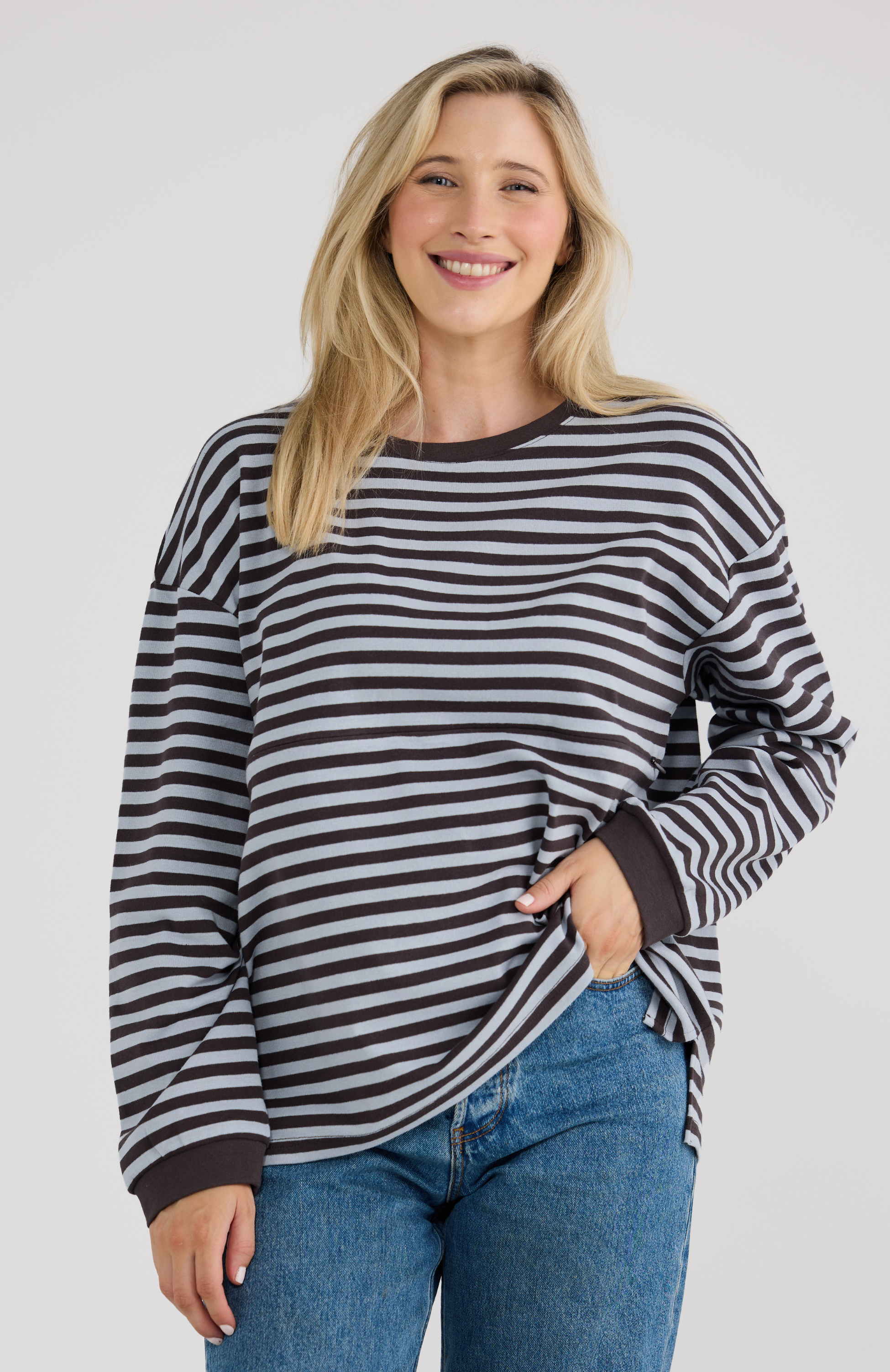 Woman wearing a blue striped sweater with blue jeans on a plain background