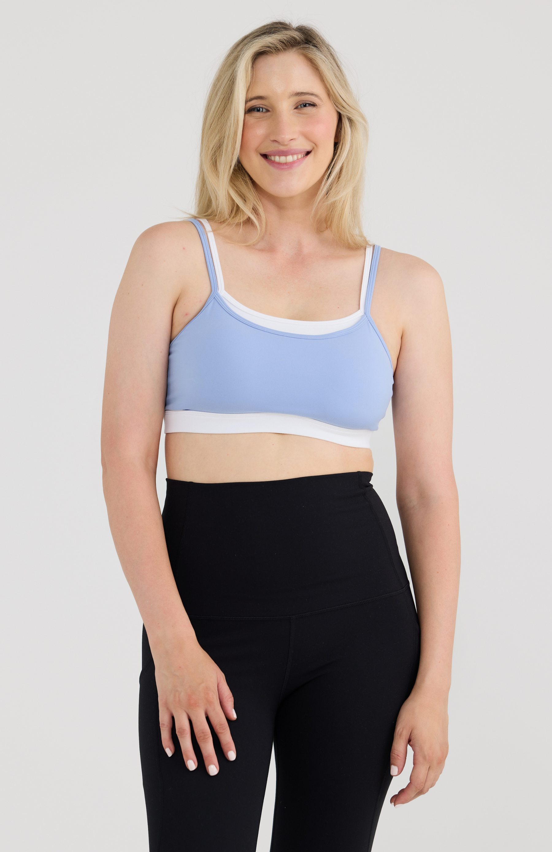 Woman wearing a light blue sports bra and black leggings on a white background
