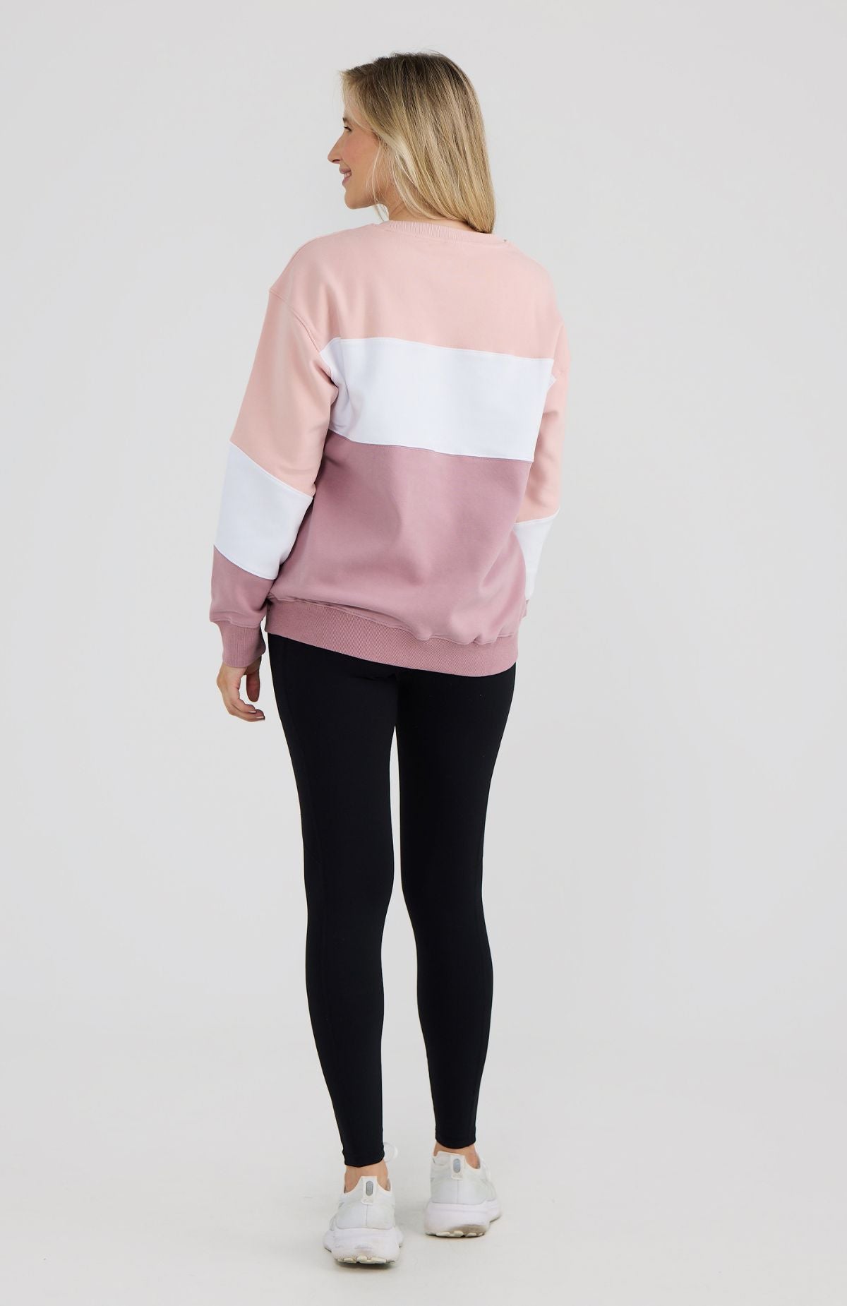 Woman wearing a pink, white, and black color-blocked sweatshirt on a light gray background