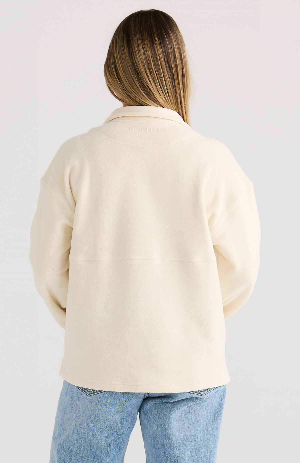 Person wearing a cream-colored jumper and blue jeans on a light gray background