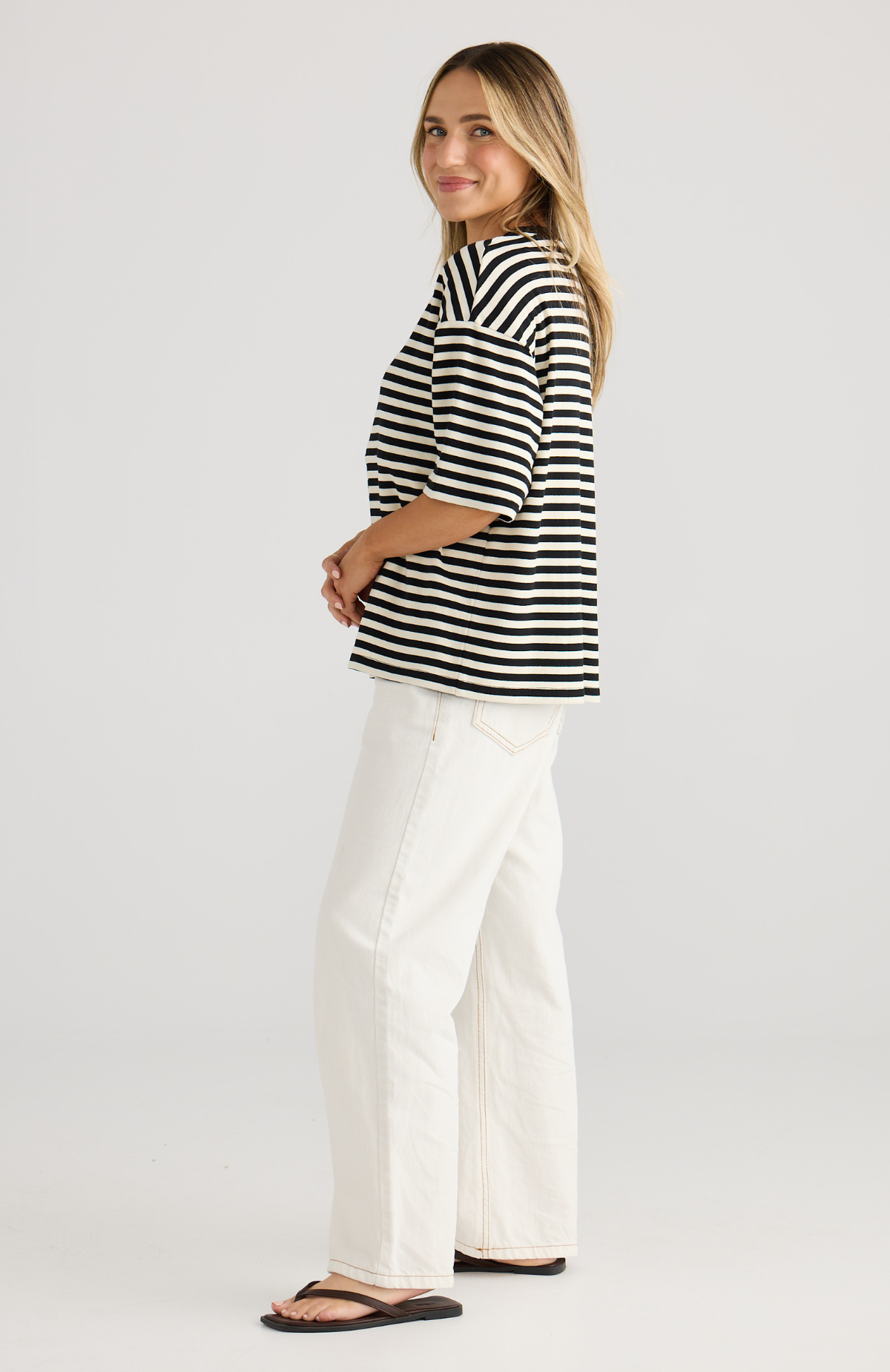 Woman wearing a black and white striped shirt and white pants on a plain background