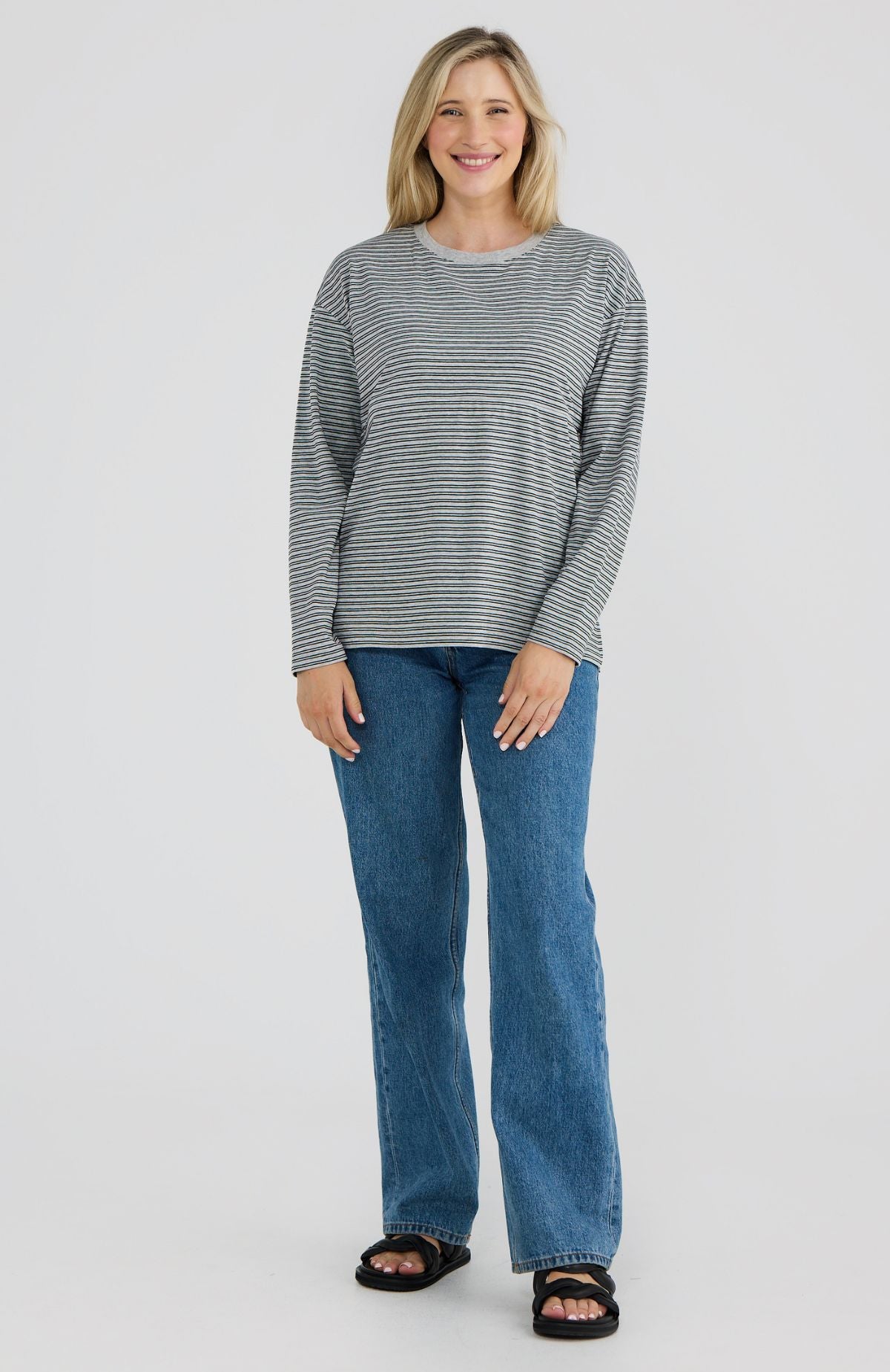 Woman wearing a striped long-sleeve top and blue jeans on a white background