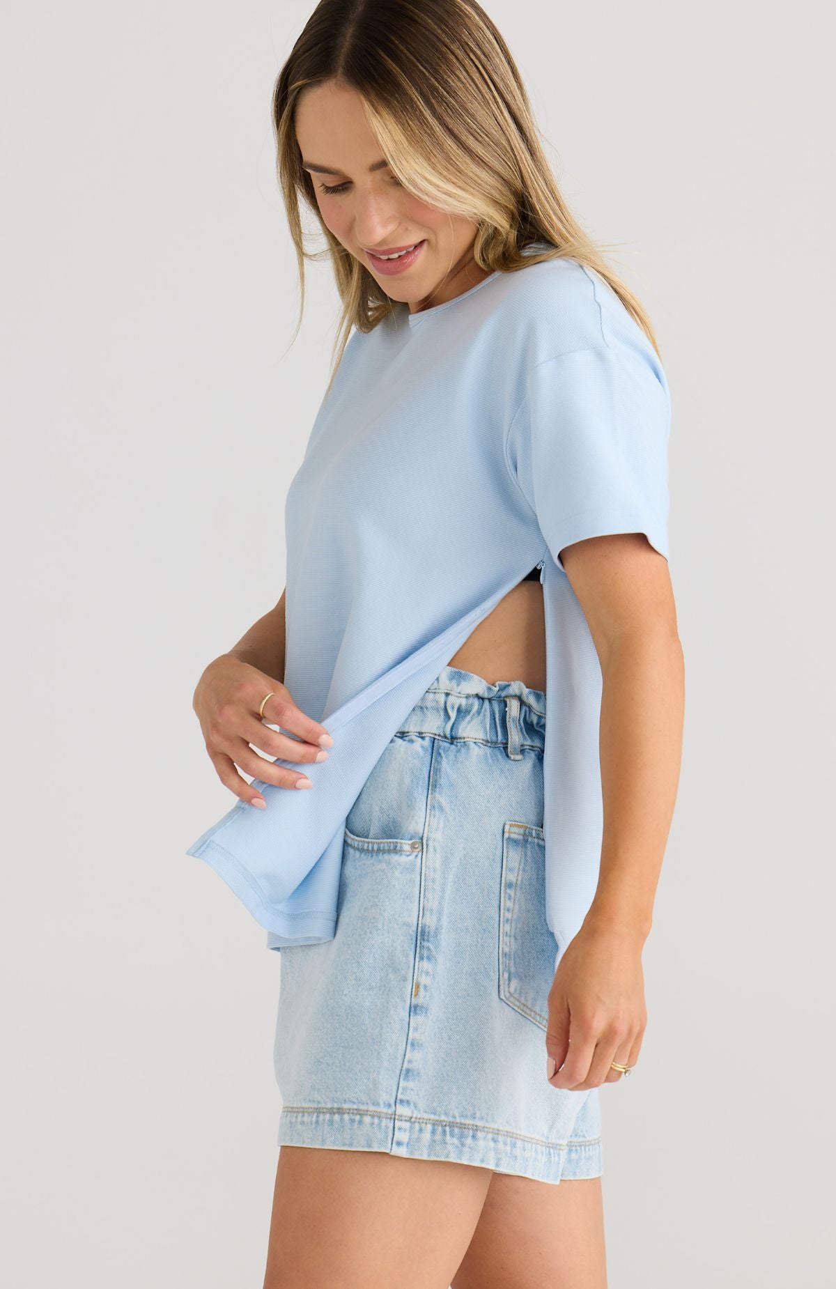 Woman wearing a light blue oversized t-shirt and denim shorts on a plain background