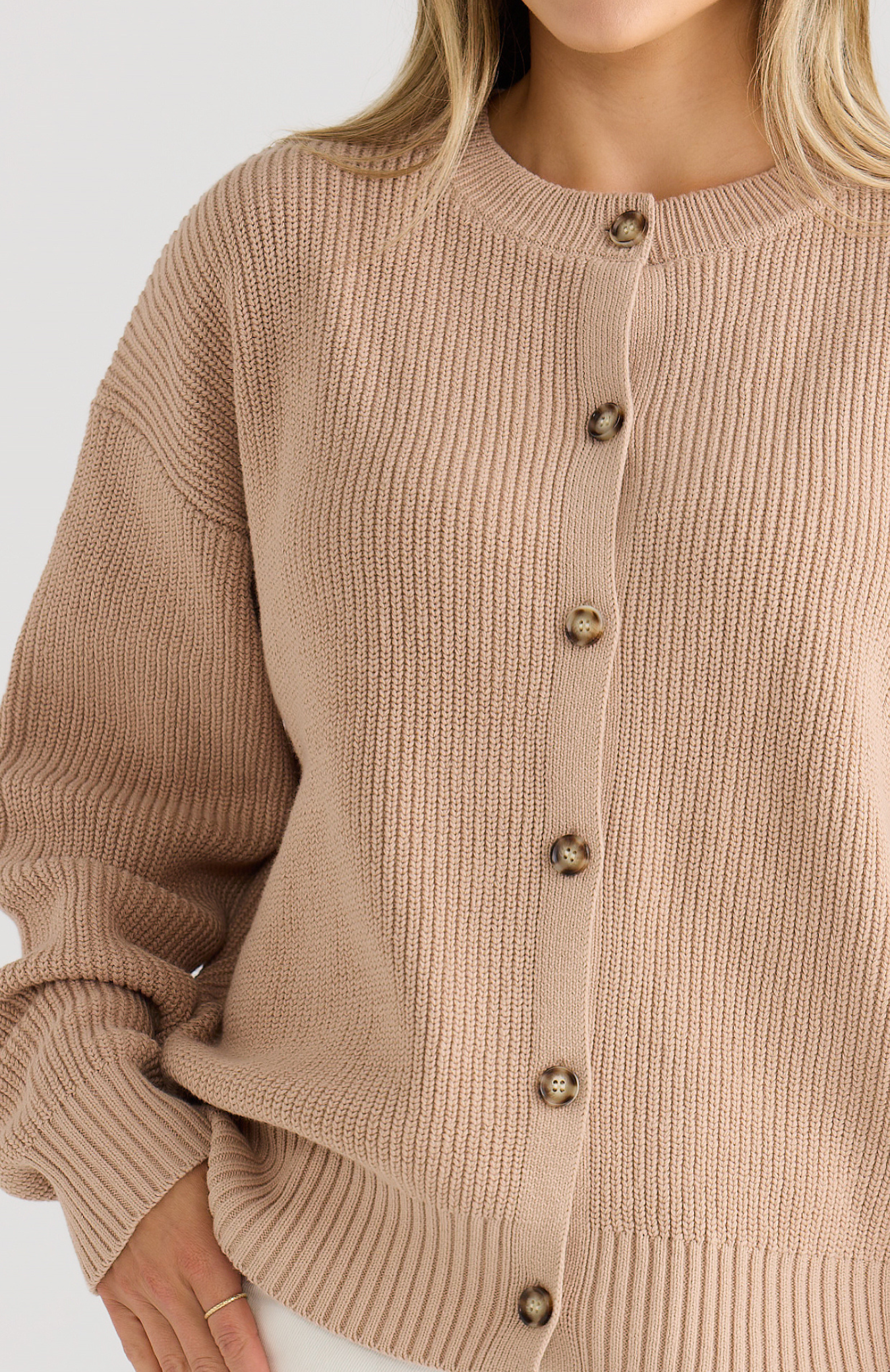 Close-up of a beige ribbed sweater with buttons on a white background