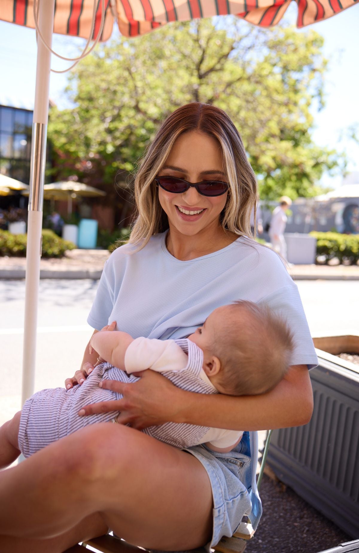 Woman breastfeeding a baby in a nursing top outdoors under an umbrella