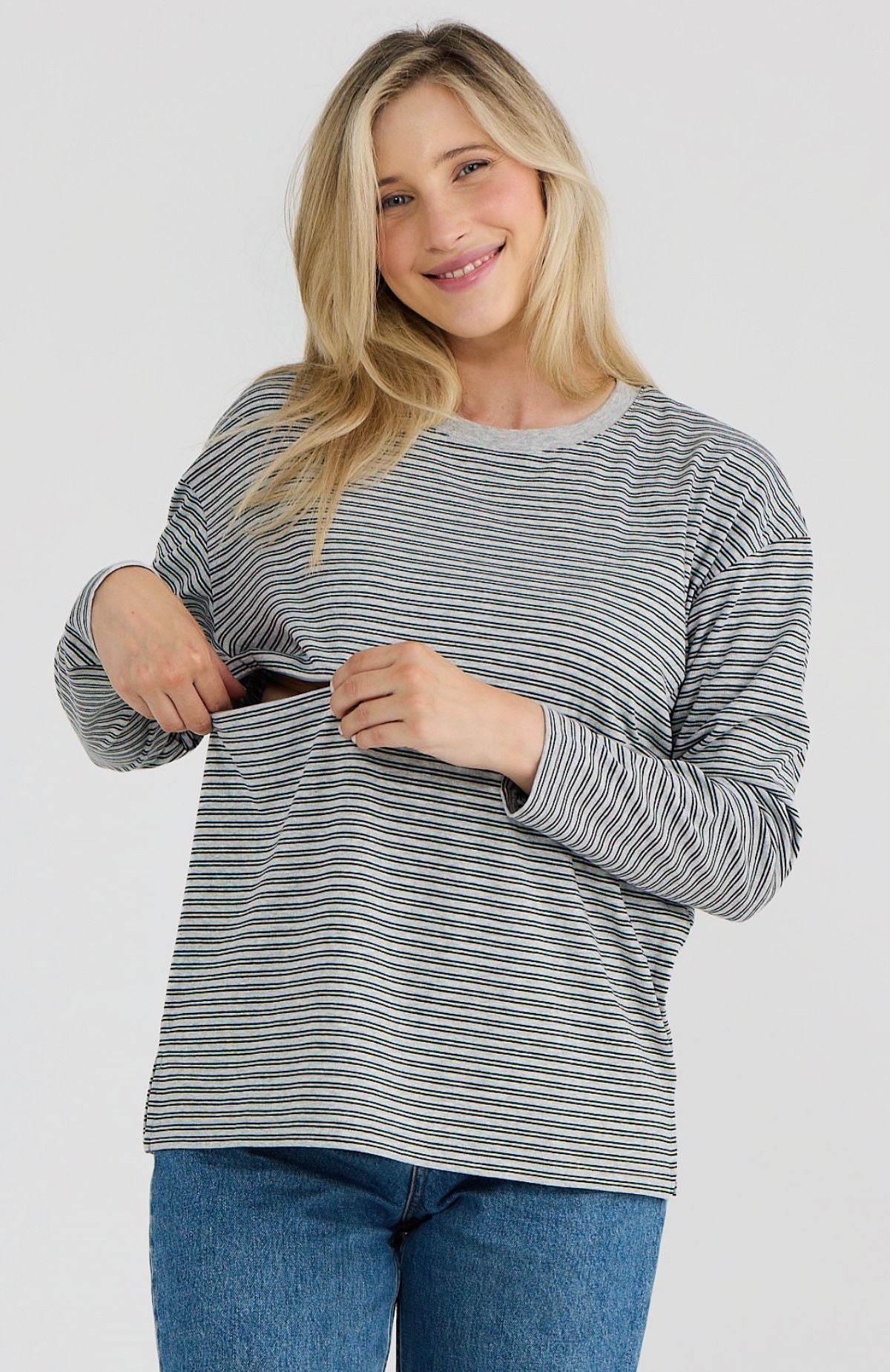 Woman wearing a striped long-sleeve top and blue jeans on a plain background