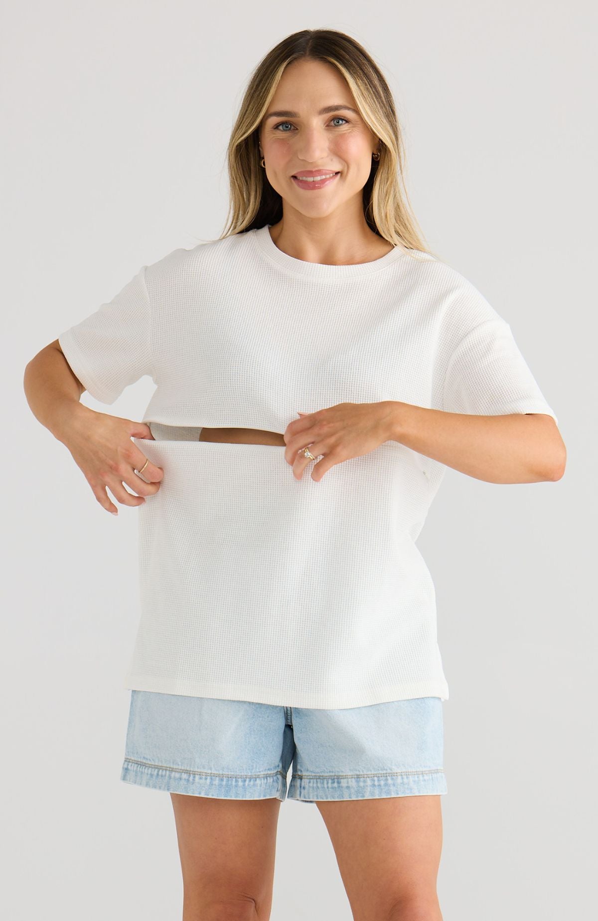 Woman wearing a white oversized shirt and light blue shorts on a plain background