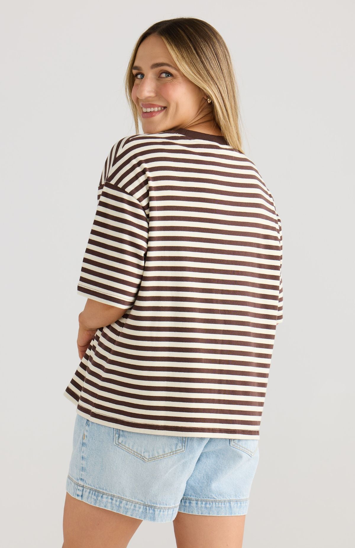 Woman wearing a brown and white striped shirt with light blue shorts on a plain background