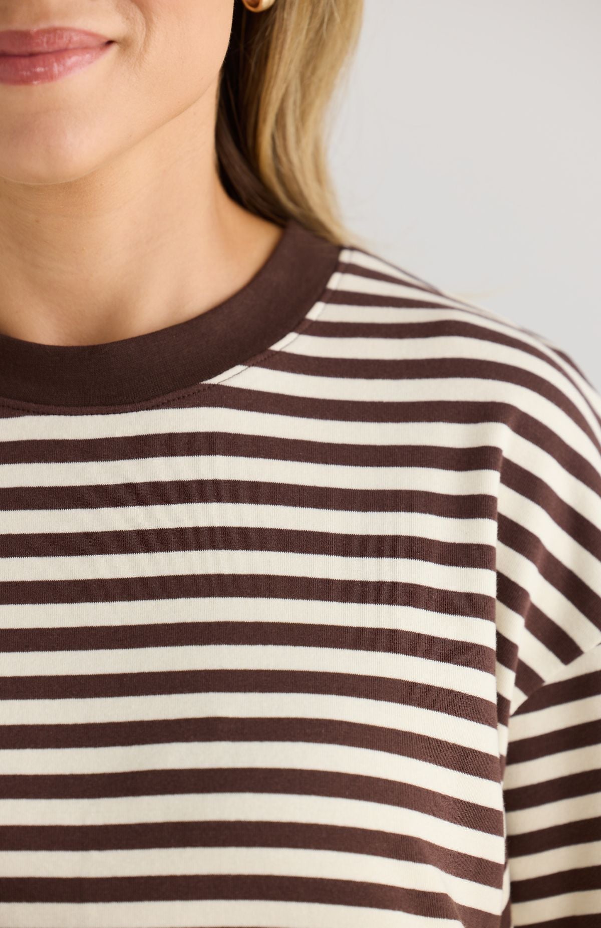 Close-up of a person wearing a brown and white striped shirt with a neutral background