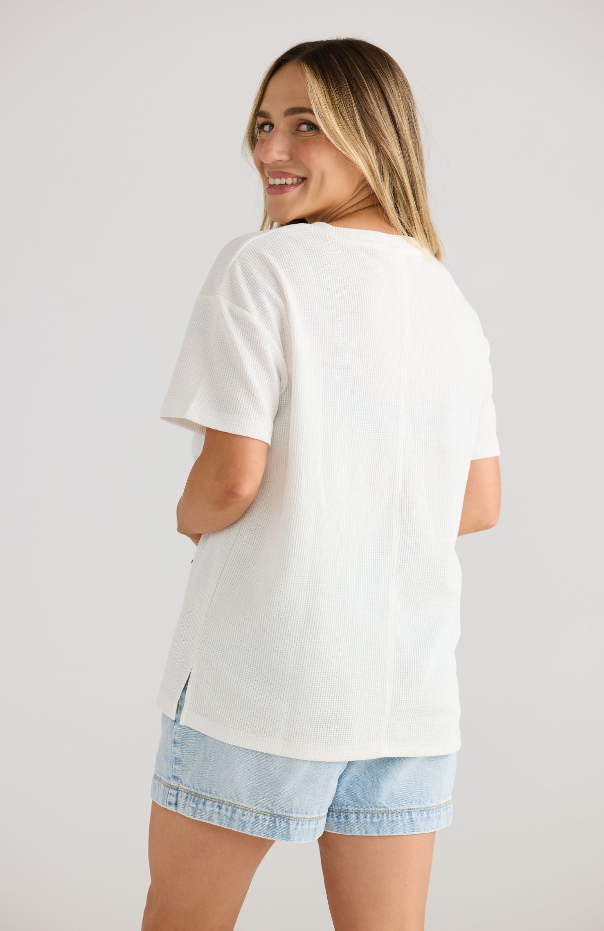 Woman wearing a white breastfeeding t-shirt and denim shorts on a plain background