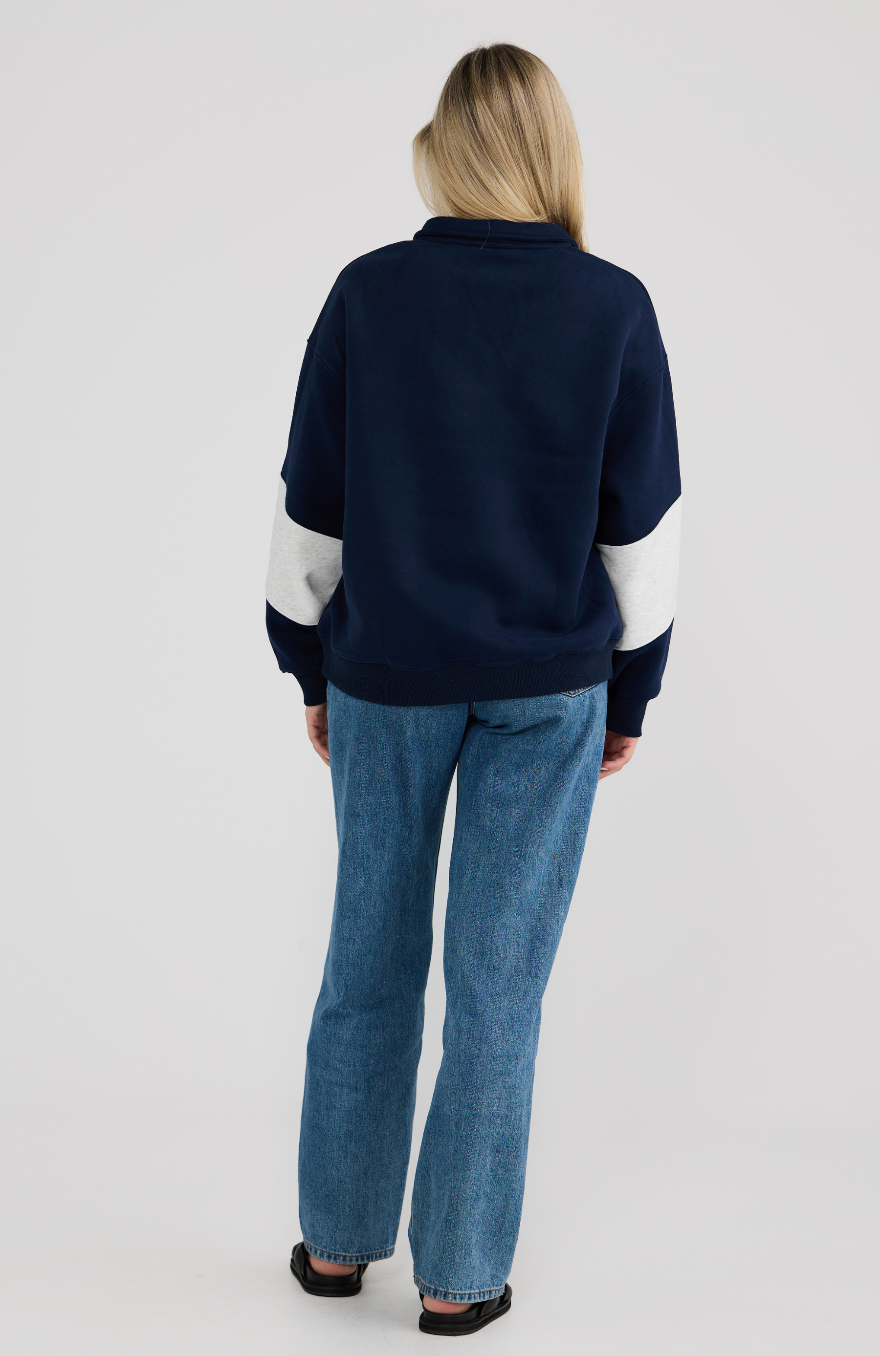 woman wearing a navy sweater with white sleeves and blue jeans on a light graey background