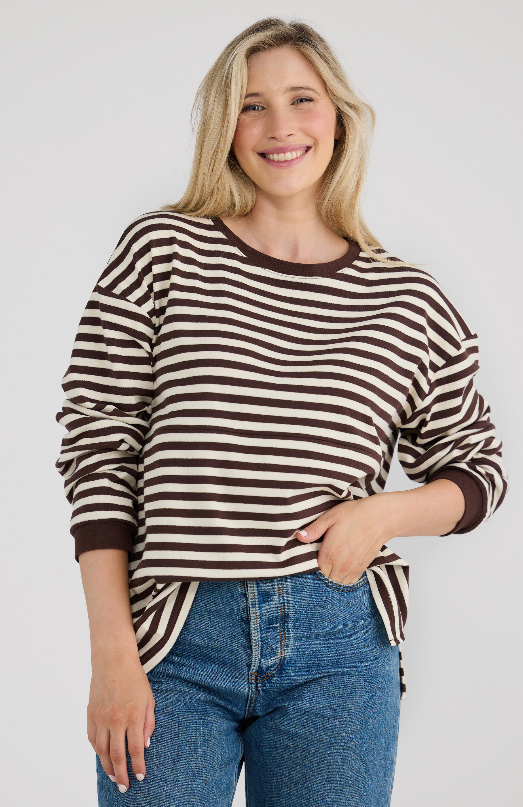 Woman wearing a brown and white striped sweater with blue jeans on a plain background