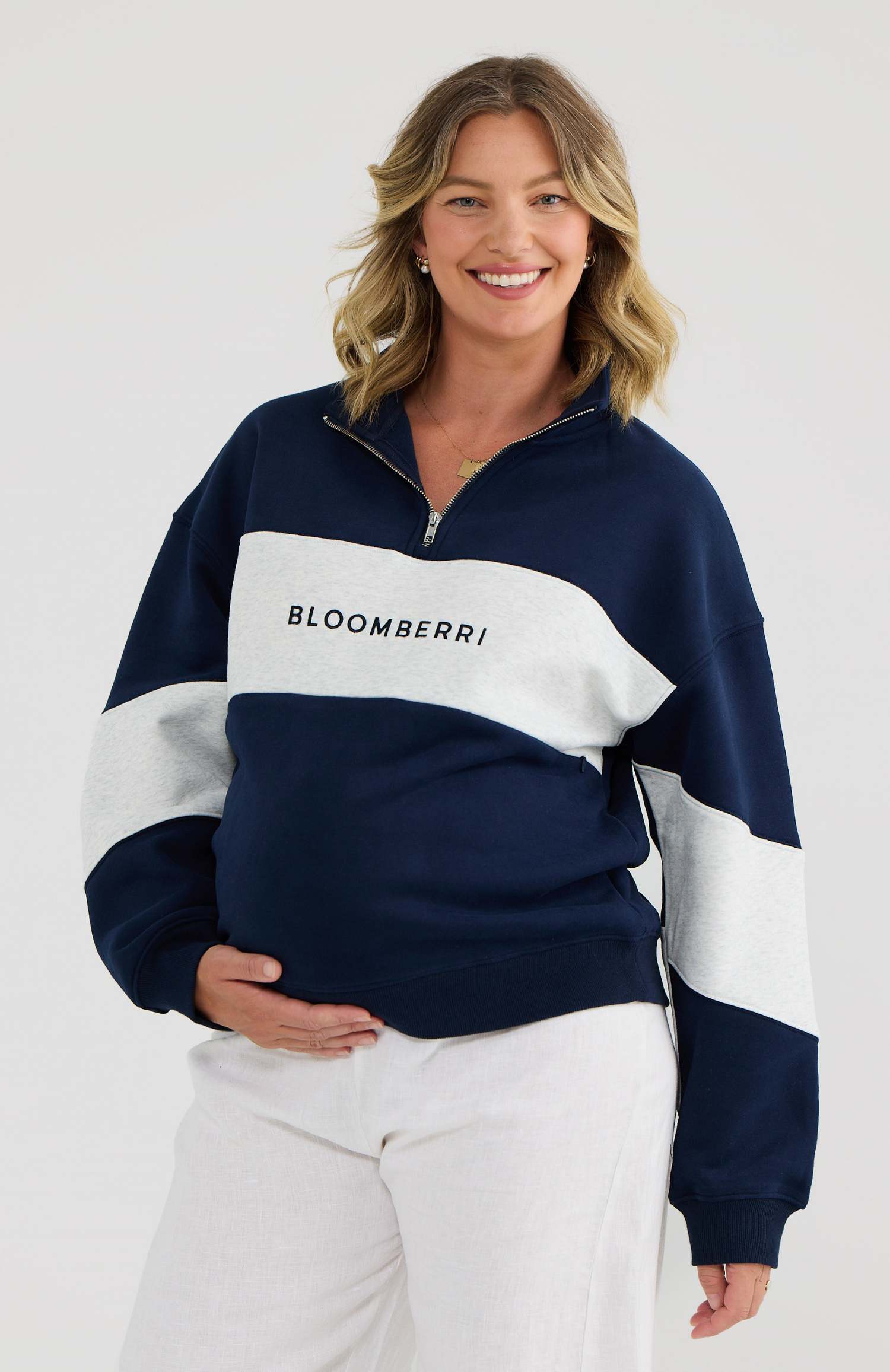 Pregnant woman wearing a navy and grey sweater on a white background