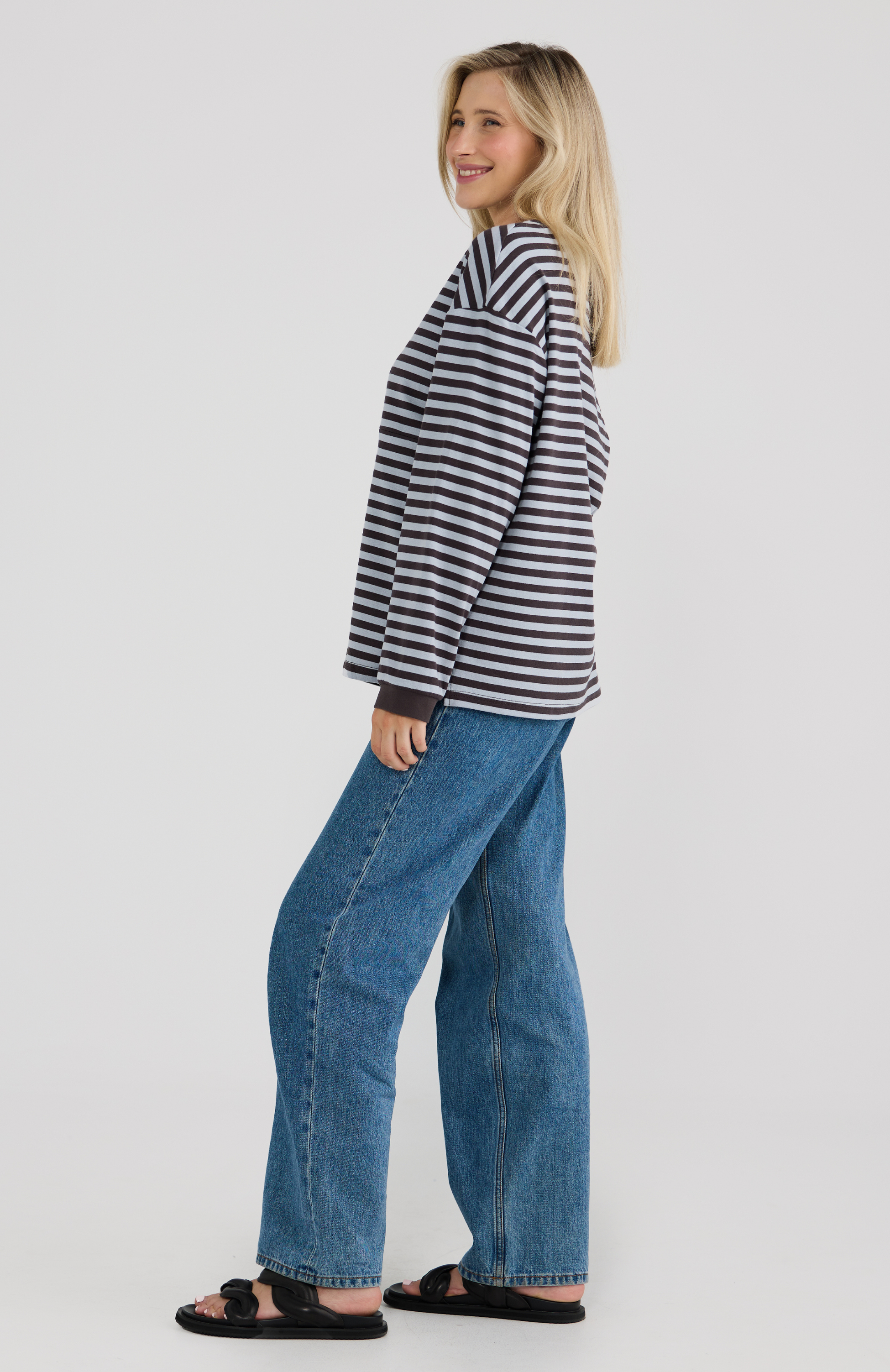 Woman wearing a striped shirt and blue jeans on a plain background