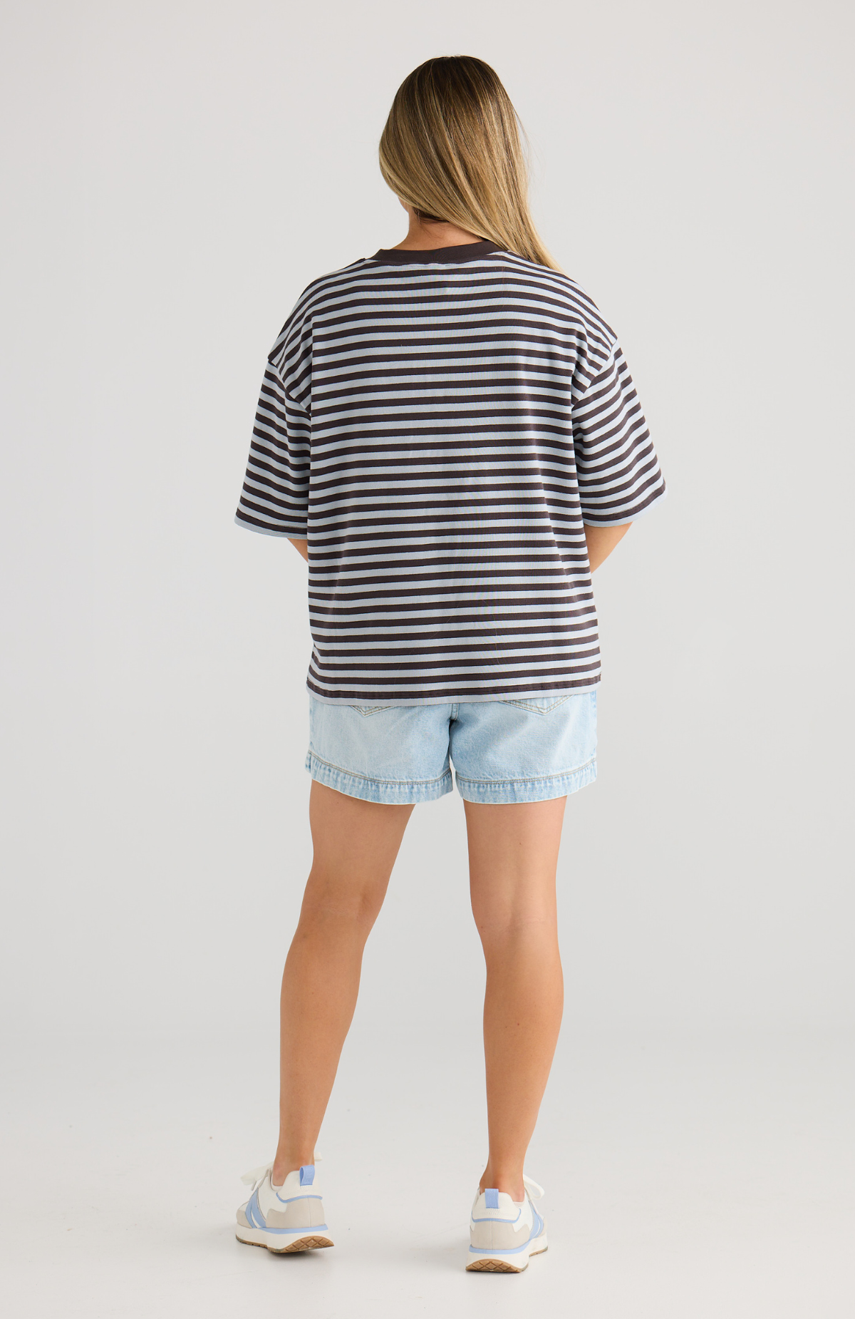 Person wearing a striped nursing top and denim shorts on a plain background