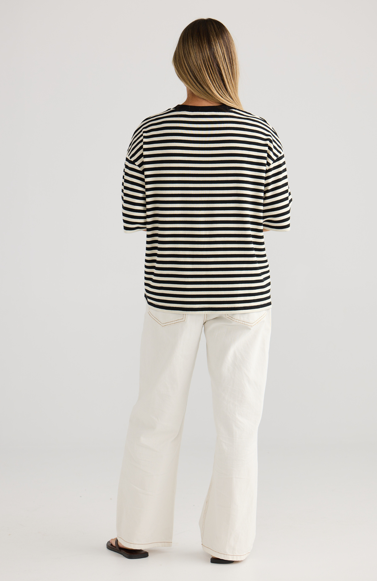 Person wearing a black and white striped shirt and white pants on a plain background