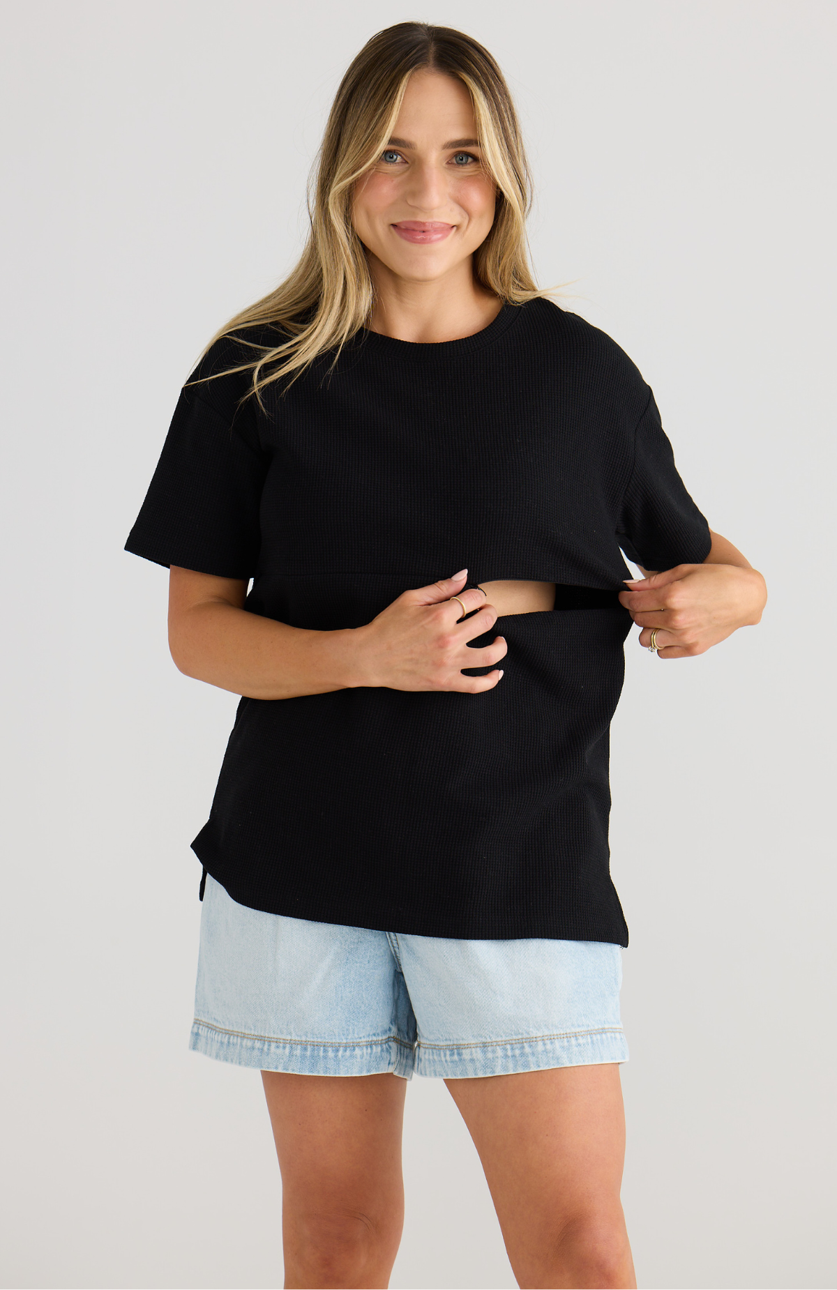 Woman wearing a black breastfeeding t-shirt and light blue shorts on a plain background