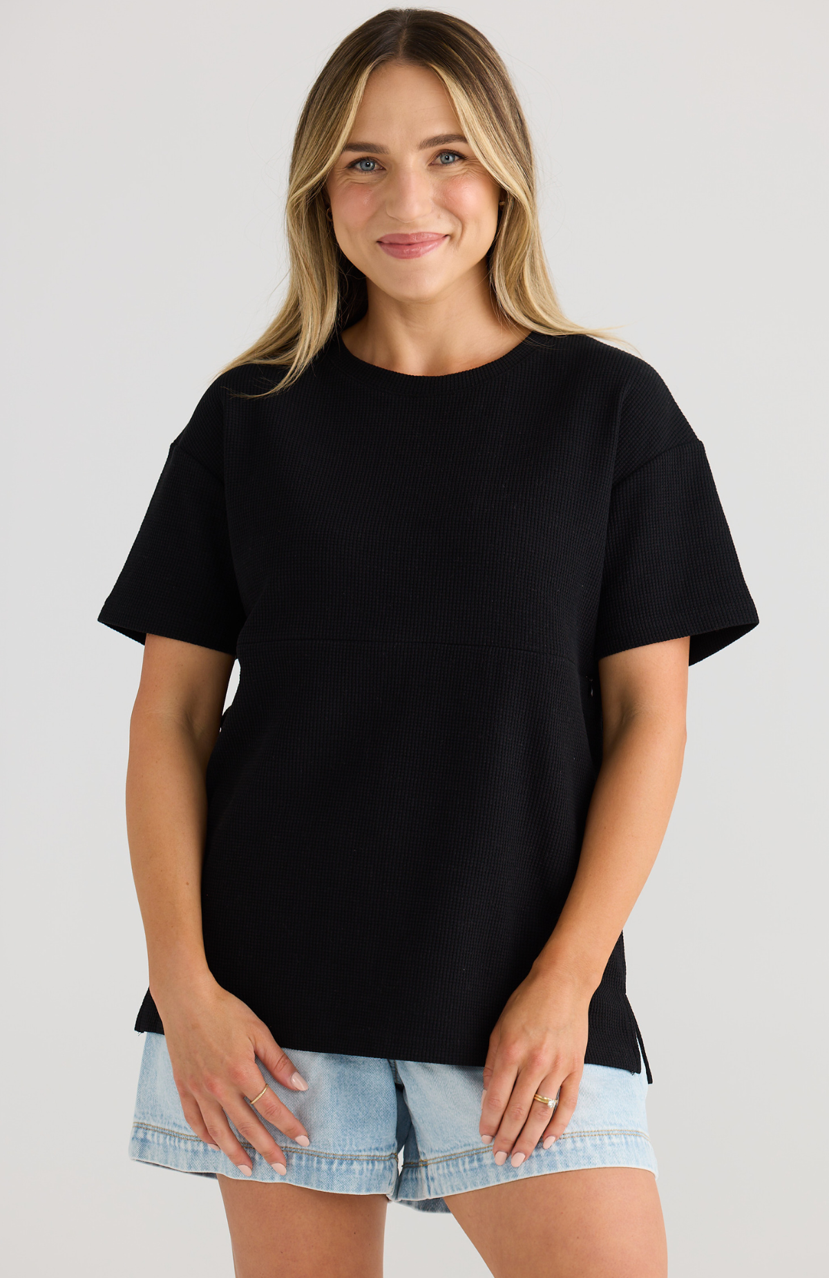 Woman wearing a black t-shirt and denim shorts on a plain background