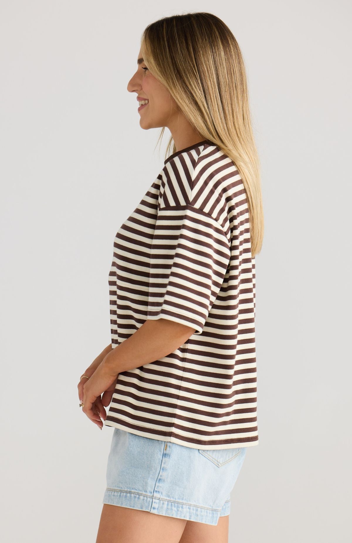 Woman wearing a brown and white striped shirt with a light blue denim skirt on a plain background