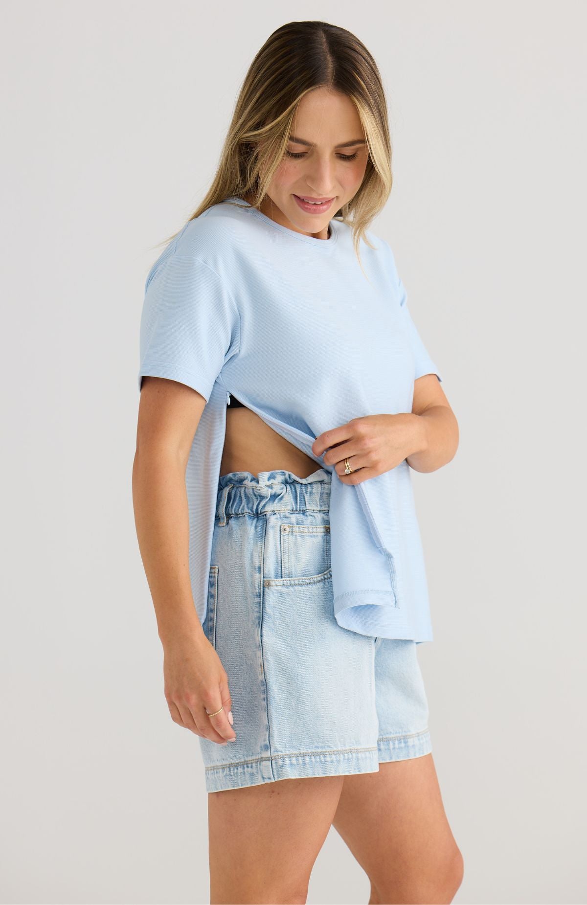 Woman wearing a light blue top and denim shorts on a plain background