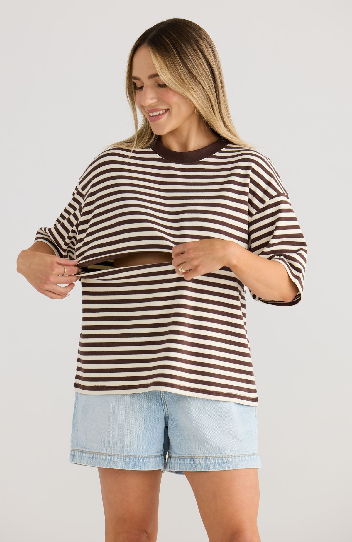 Woman wearing a brown and white striped top with light blue shorts on a plain background