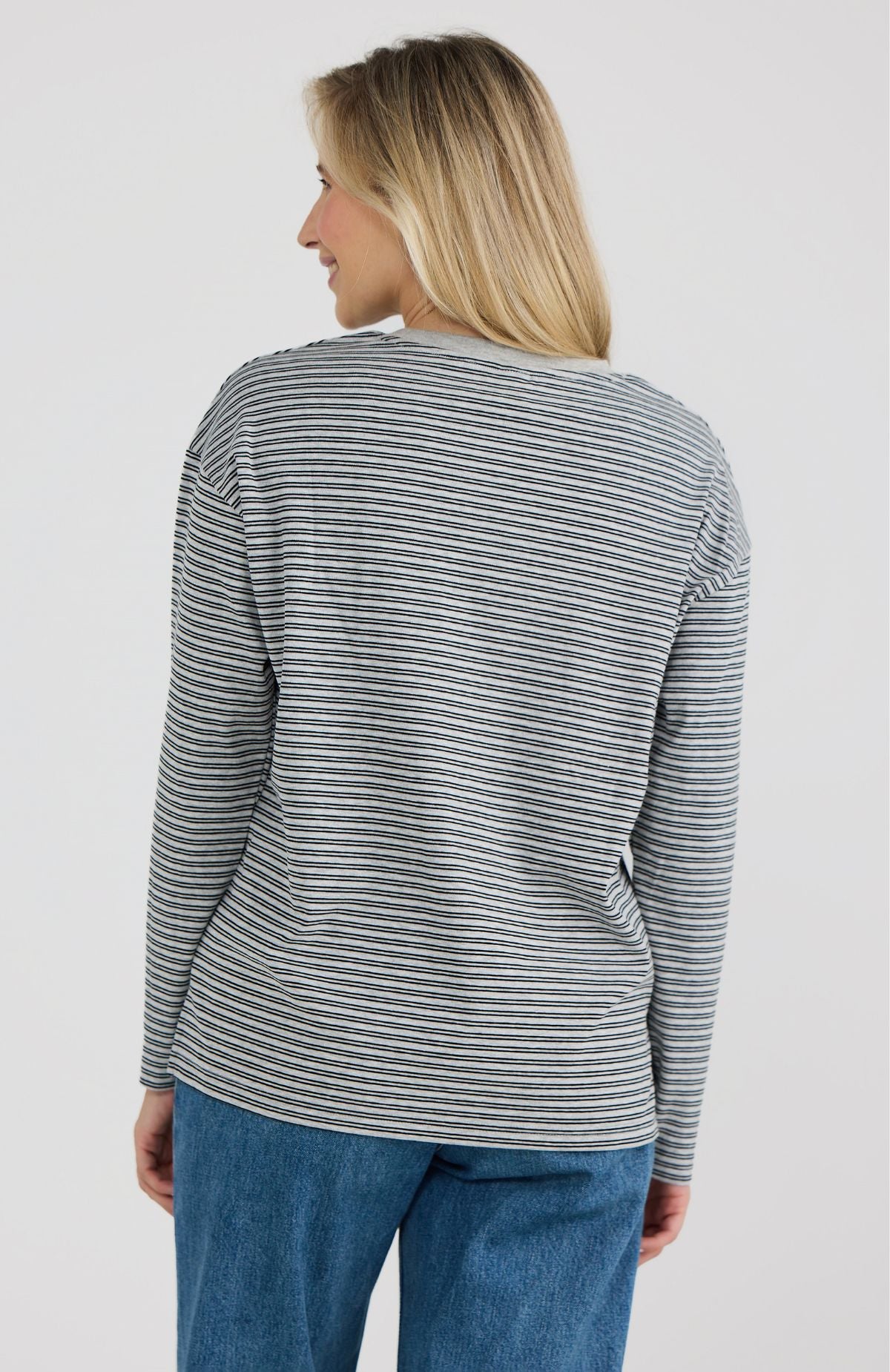 Woman wearing a striped long-sleeve shirt and blue jeans on a plain background