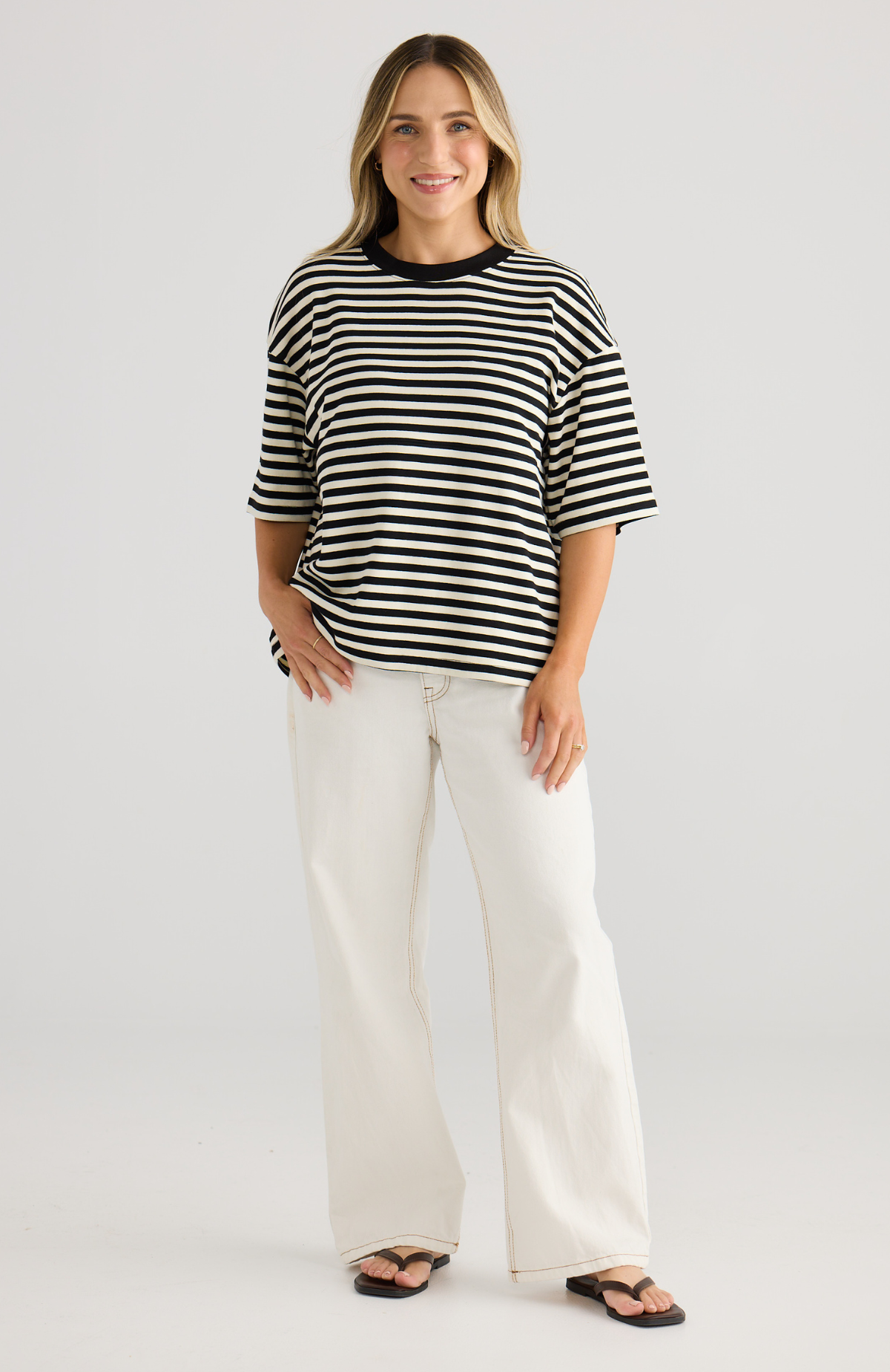 Woman wearing a black and white striped top and white pants on a plain background