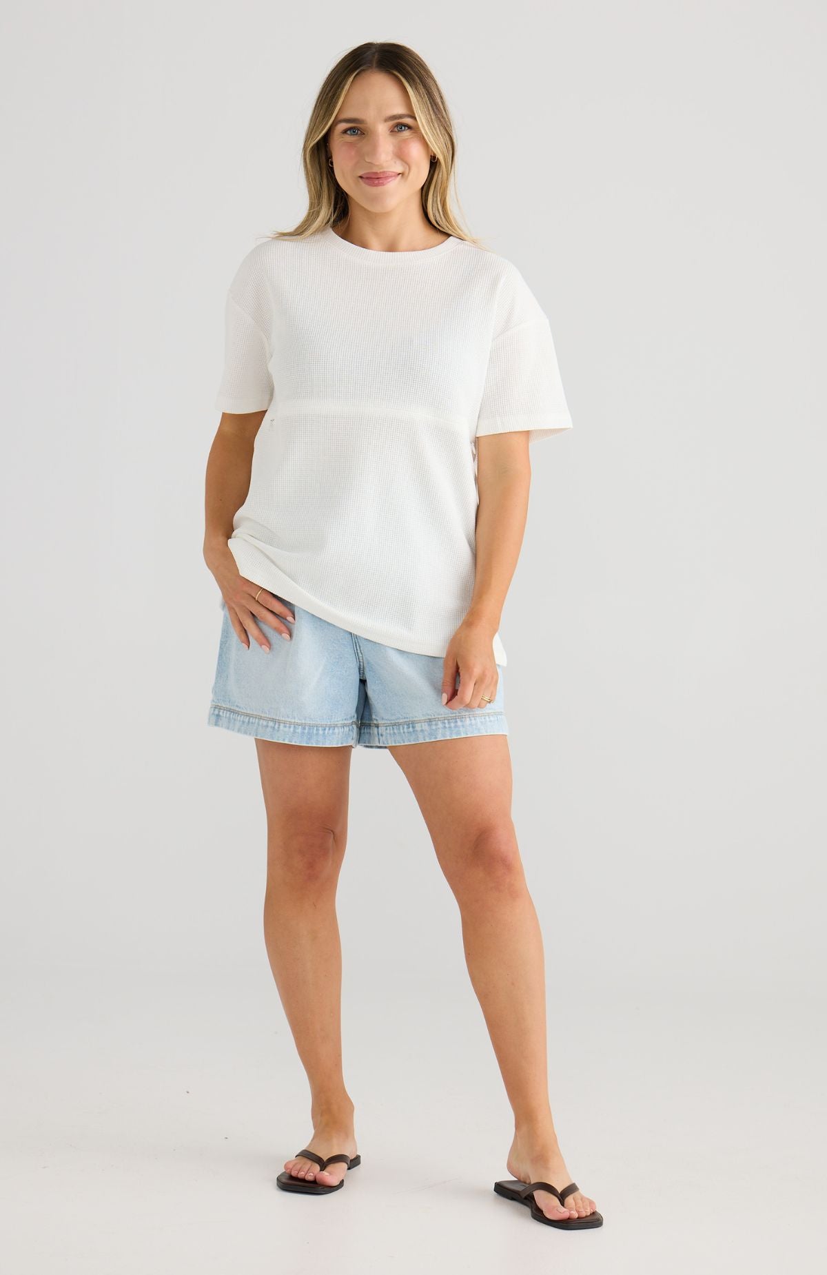 Woman wearing a white top and light blue denim shorts on a plain background