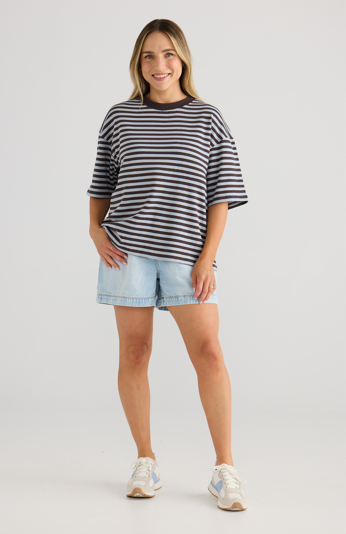 Woman wearing a striped shirt and denim shorts on a plain background