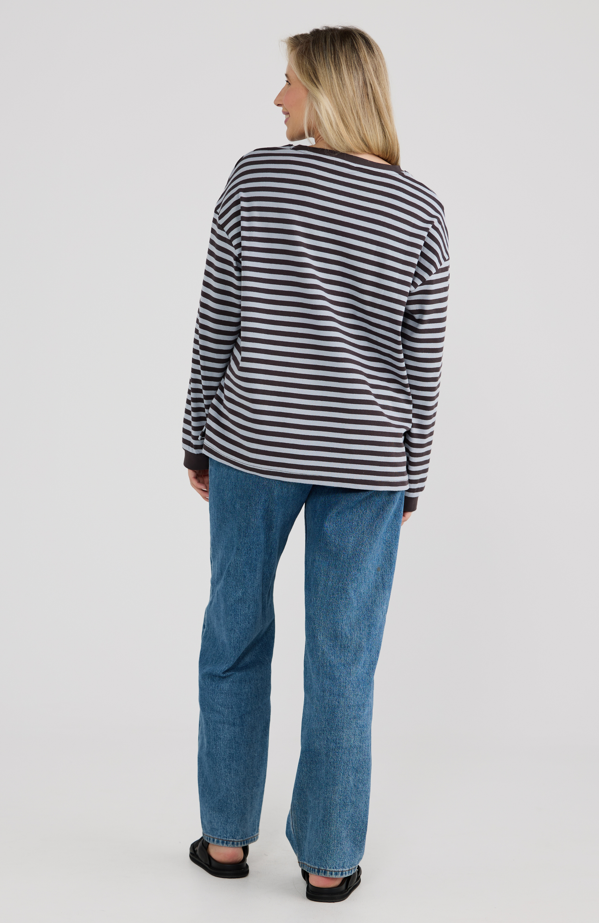 Woman wearing a striped shirt and blue jeans on a plain background