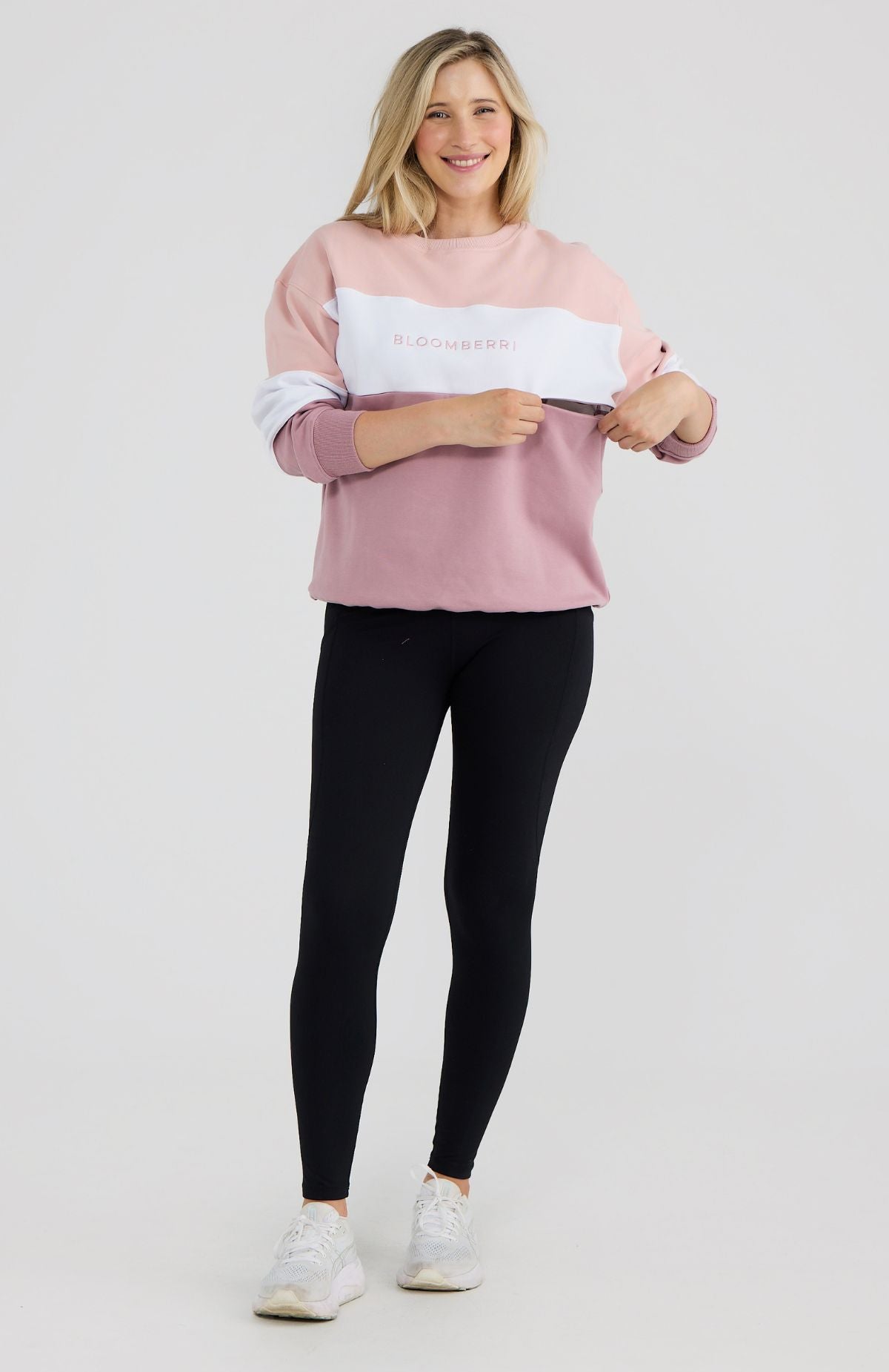 Woman wearing a pink and white sweatshirt with black leggings on a light gray background