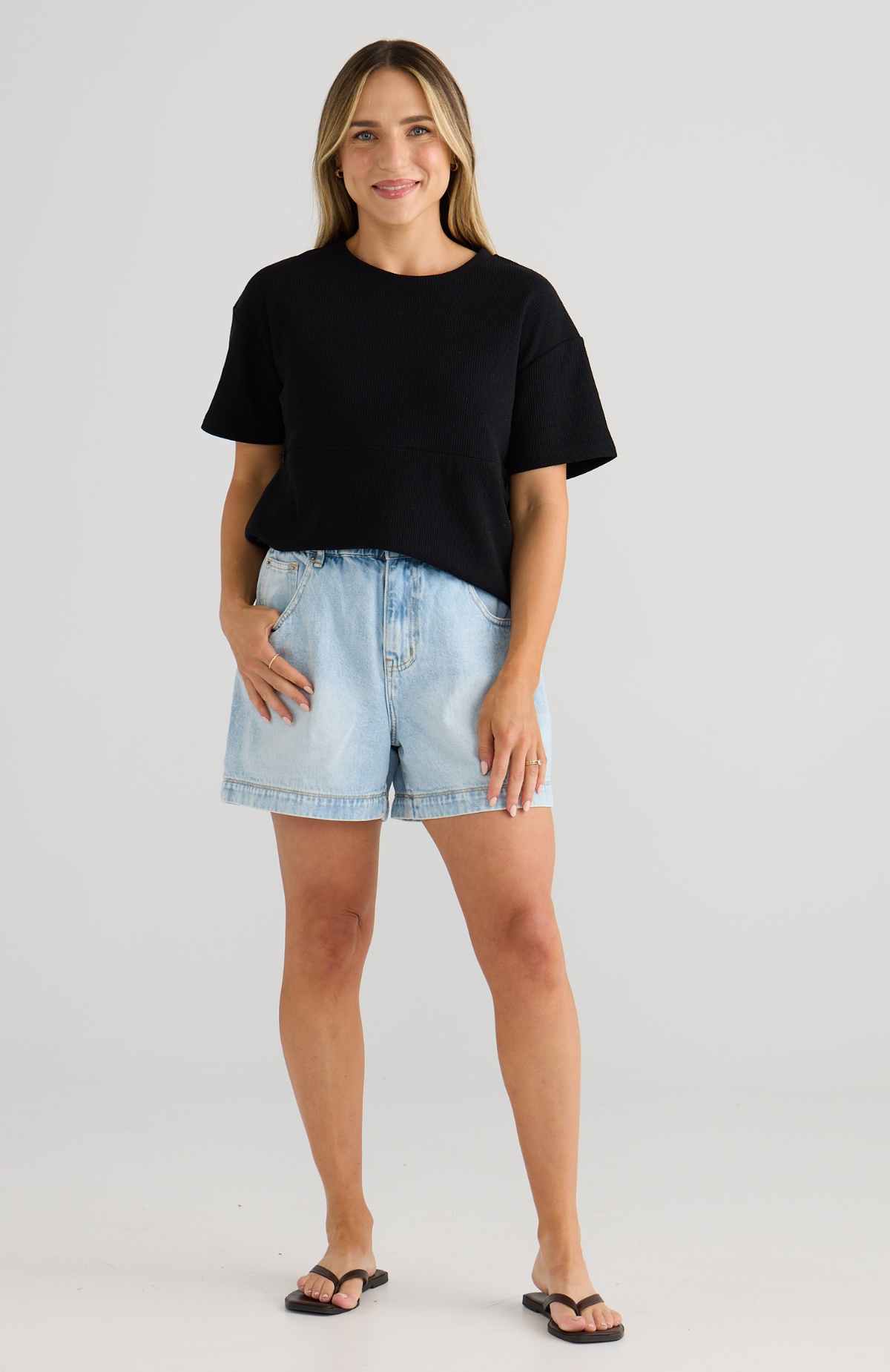 Woman wearing a black breastfeeding t-shirt and light blue denim shorts on a white background
