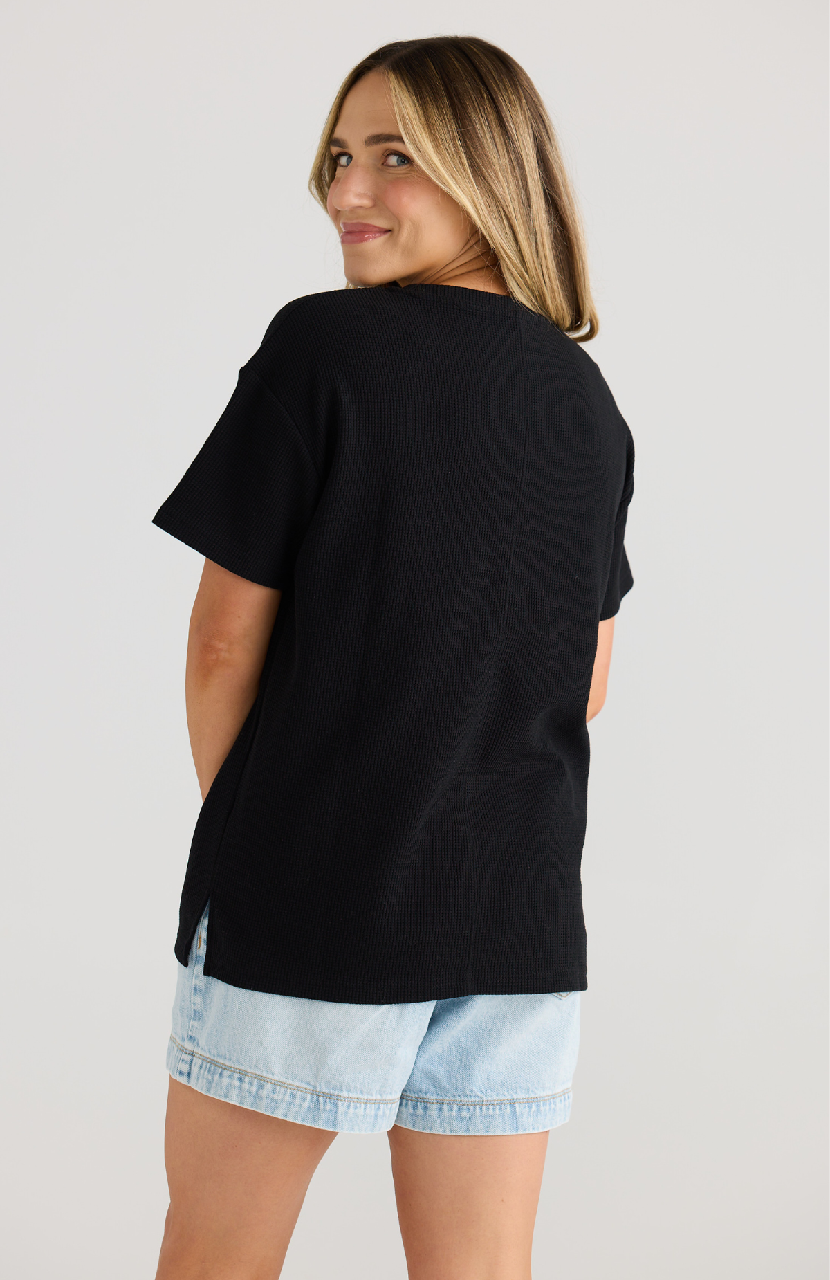 Woman wearing a black breastfeeding t-shirt and denim shorts on a plain background