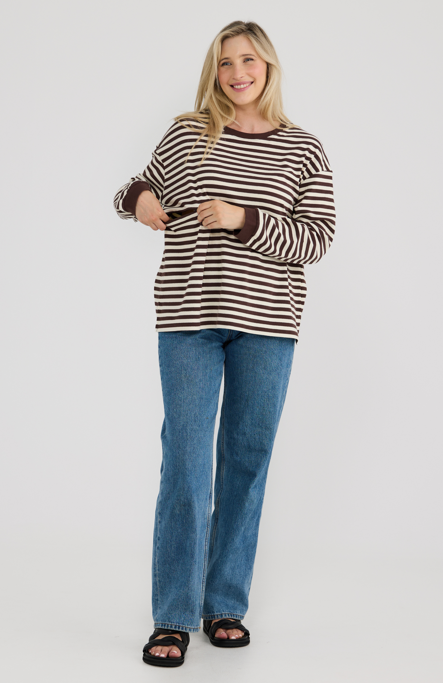 Woman wearing a brown and white striped top and blue jeans on a white background