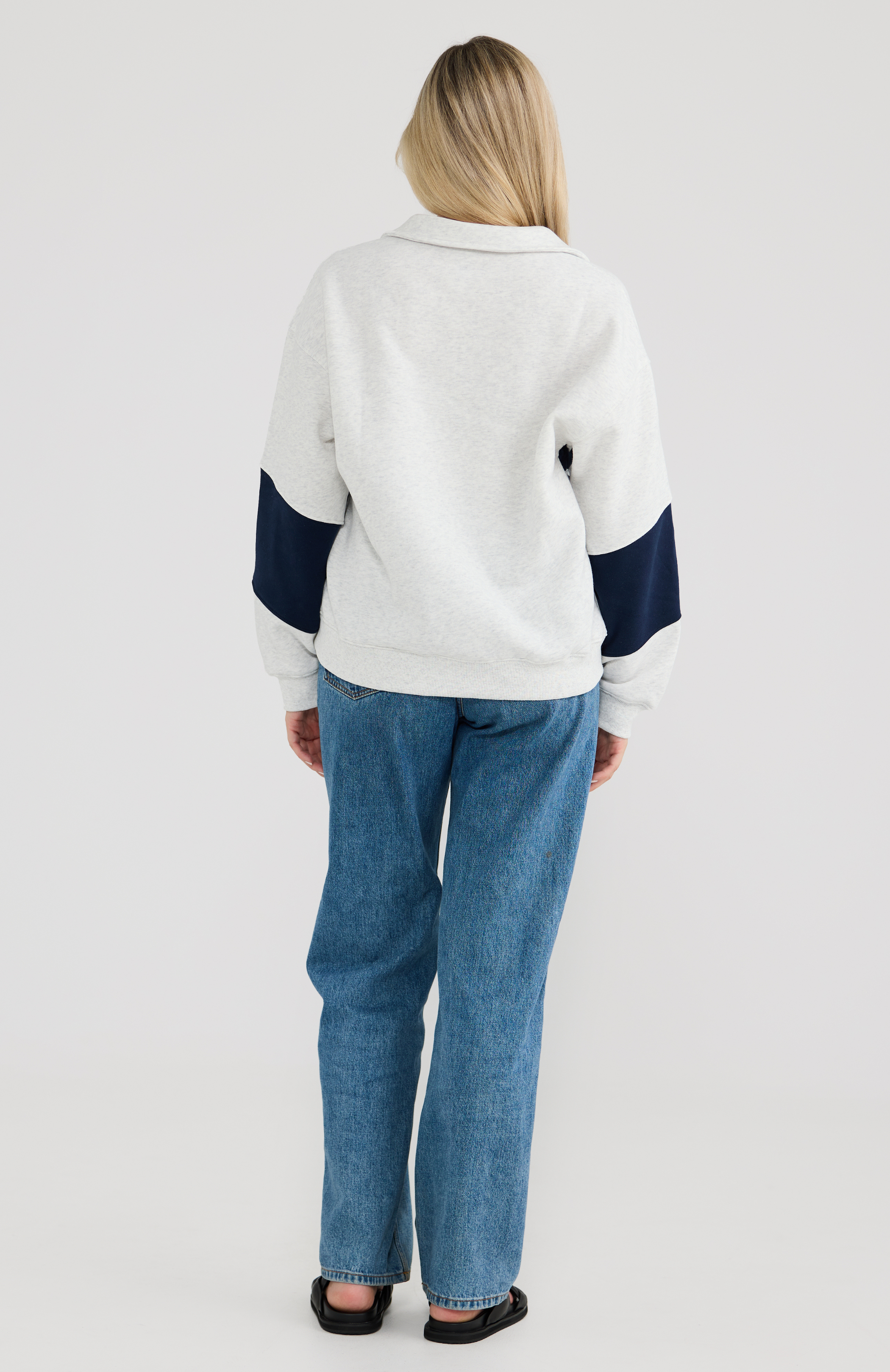 Woman wearing a grey and navy sweater with blue jeans on a light grey background
