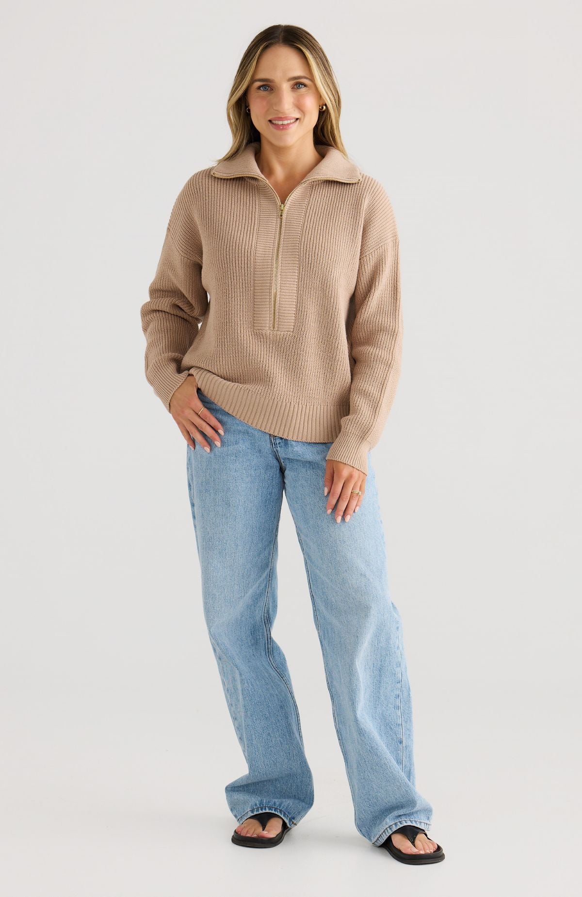 Woman wearing a beige sweater and light blue jeans on a white background