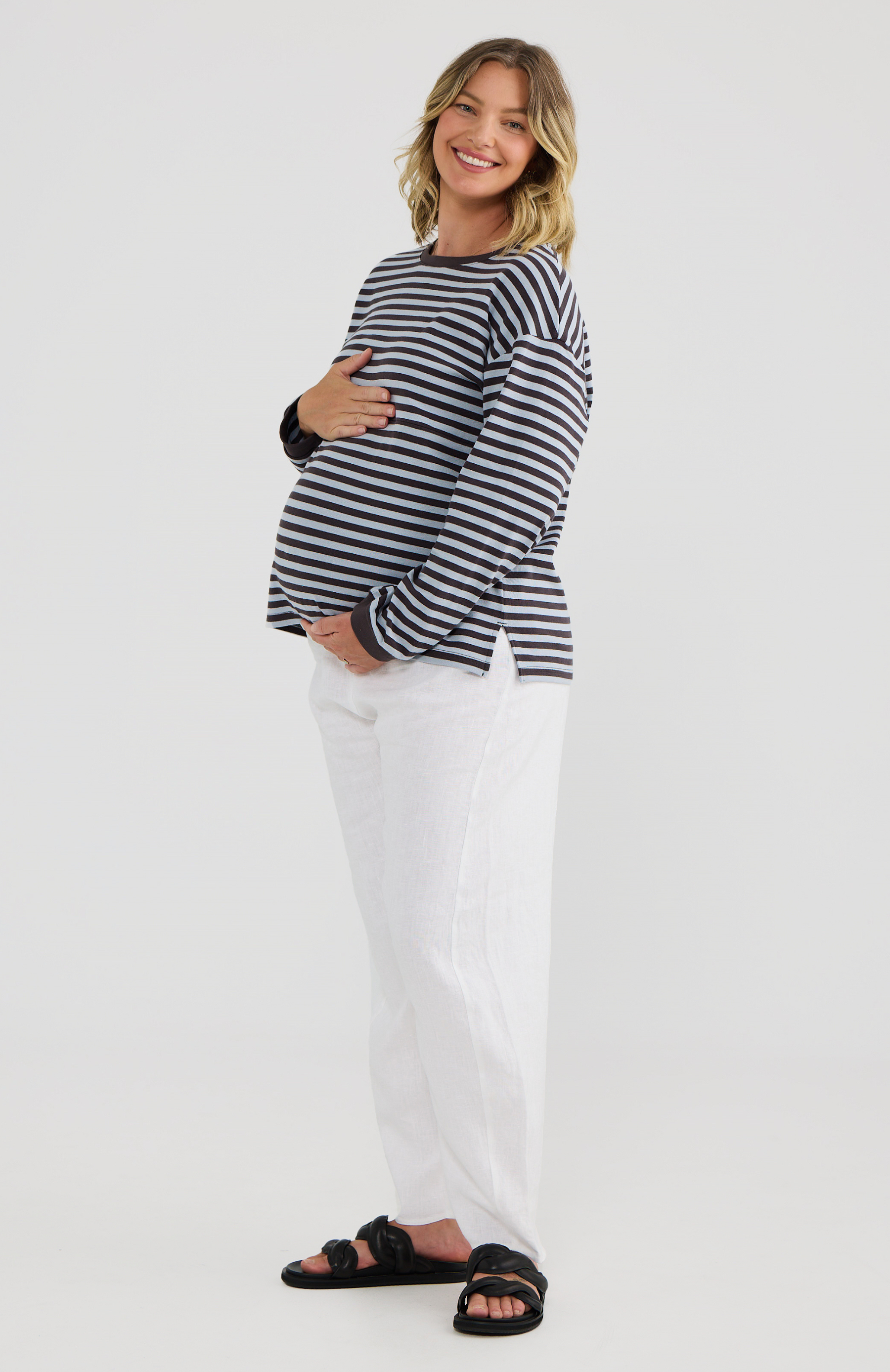 Pregnant woman wearing a striped shirt and white pants on a white background
