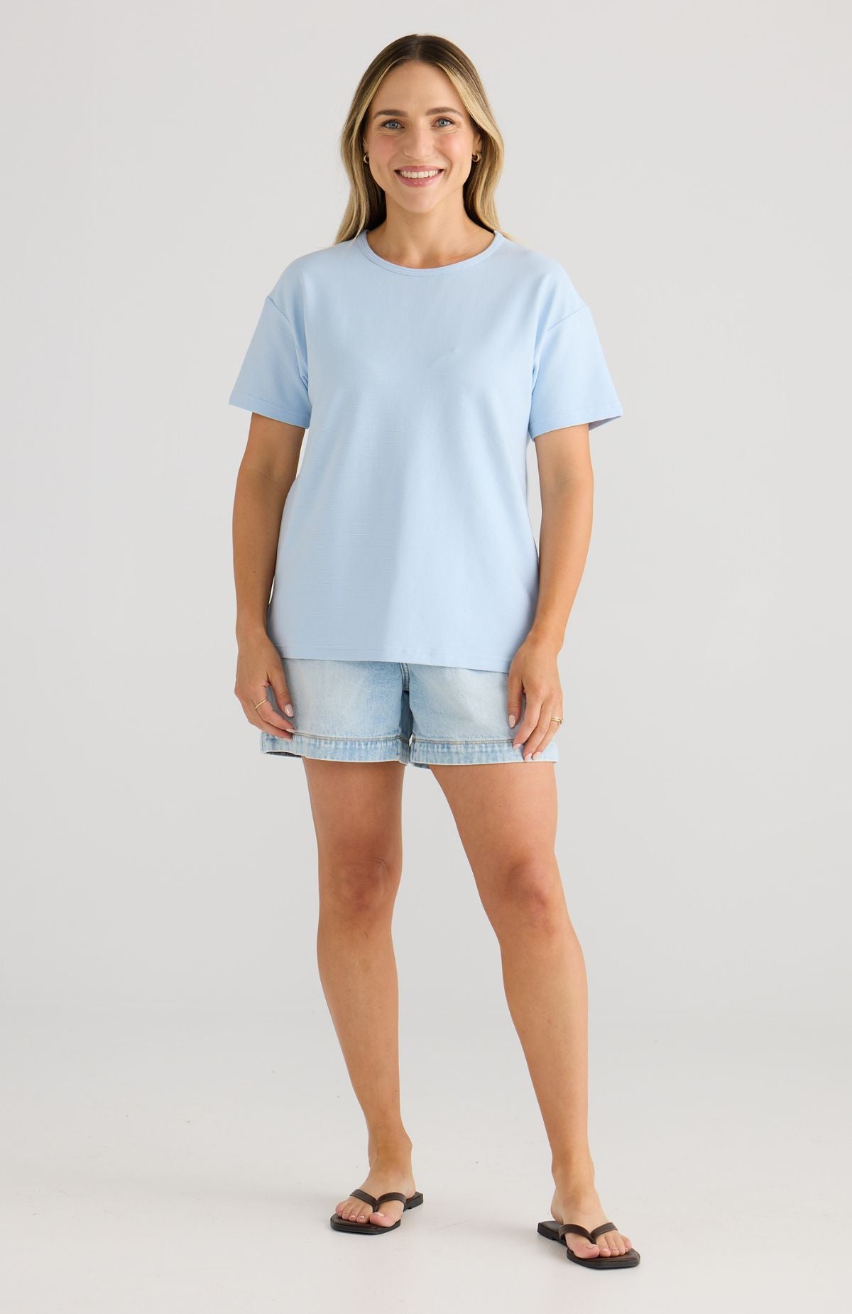 Woman wearing a light blue t-shirt and denim shorts on a plain background