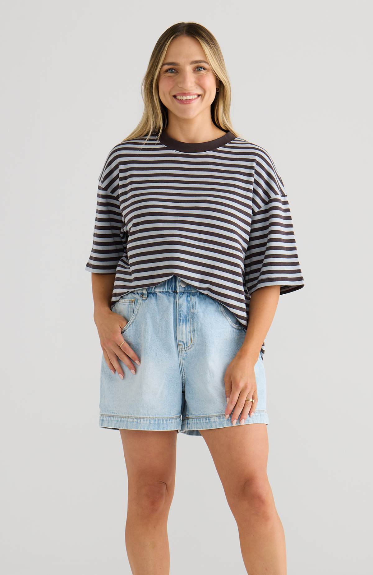Woman wearing a striped shirt and denim shorts on a plain background