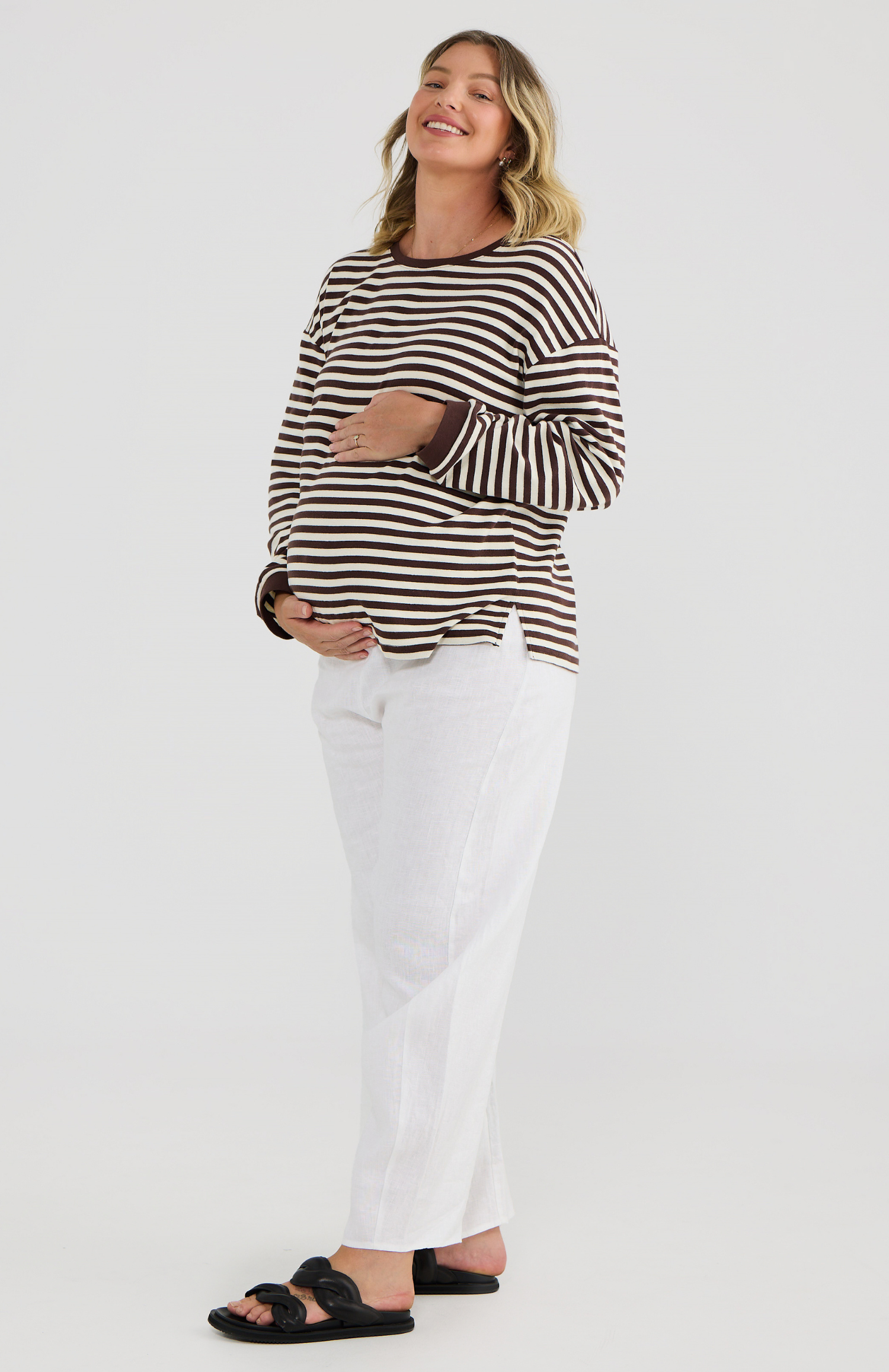 Pregnant woman wearing a brown and white striped shirt and white pants on a white background