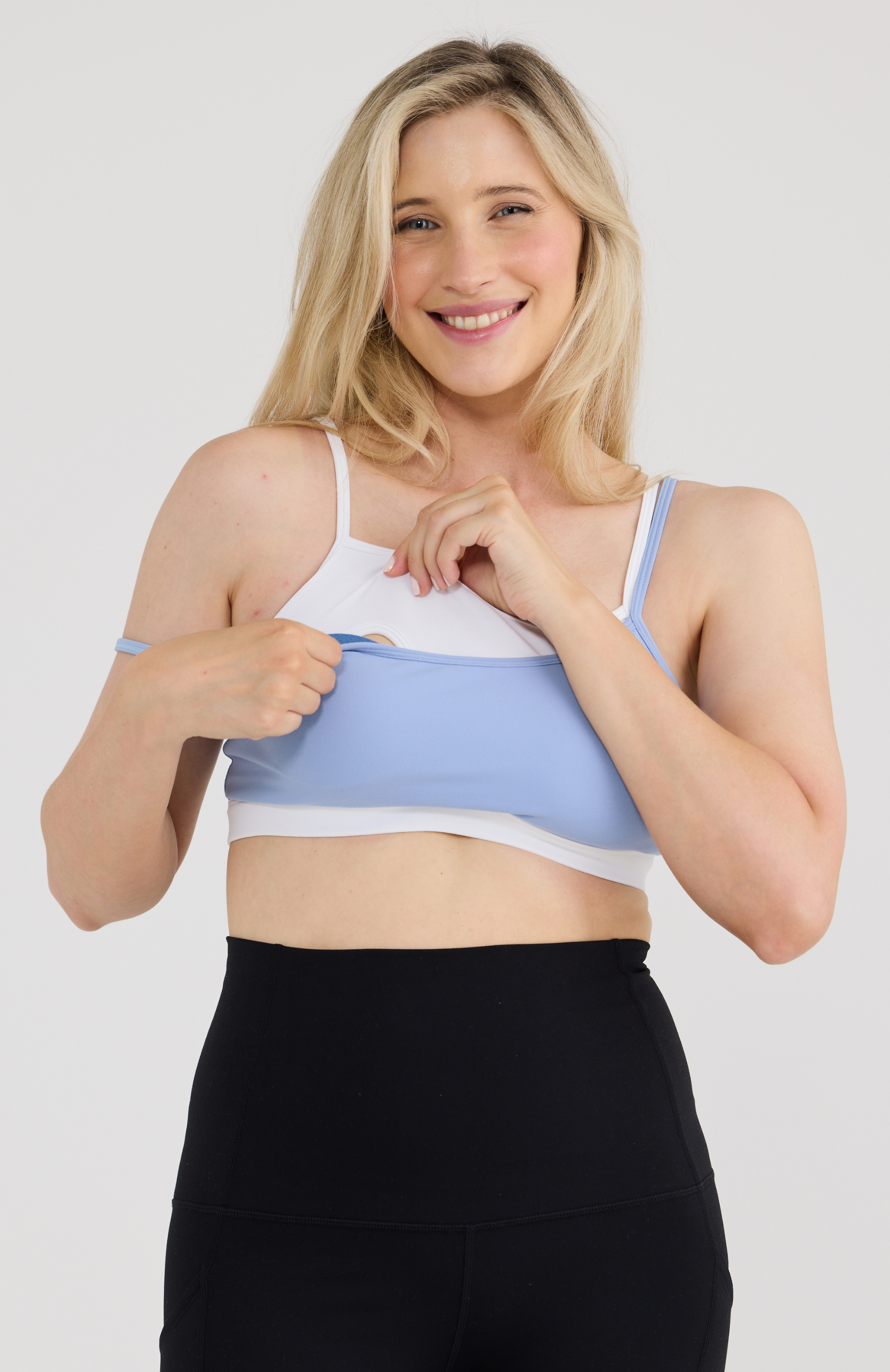 Woman wearing a two-tone sports bra and black leggings on a plain background