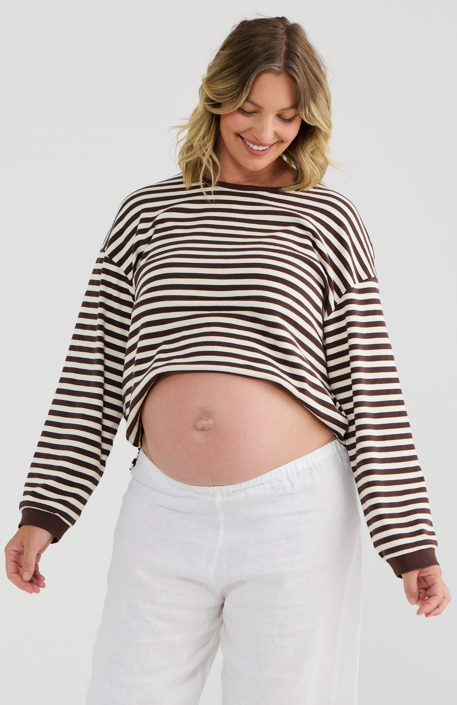 Woman wearing a striped sweater and white pants on a plain background