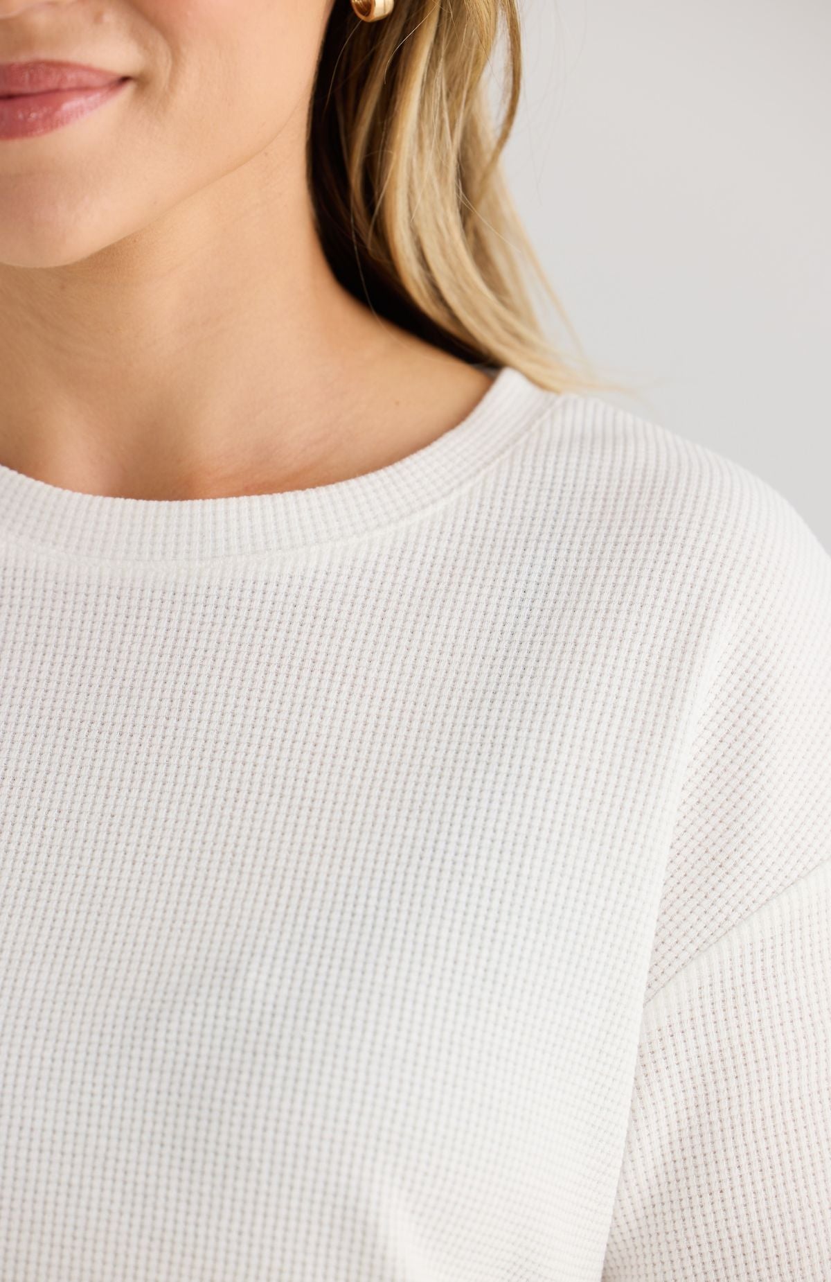 Close-up of a person wearing a white textured waffle top against a neutral background