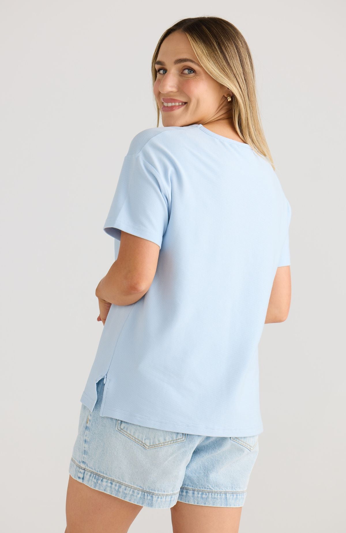 Woman wearing a light blue t-shirt and denim shorts on a plain background