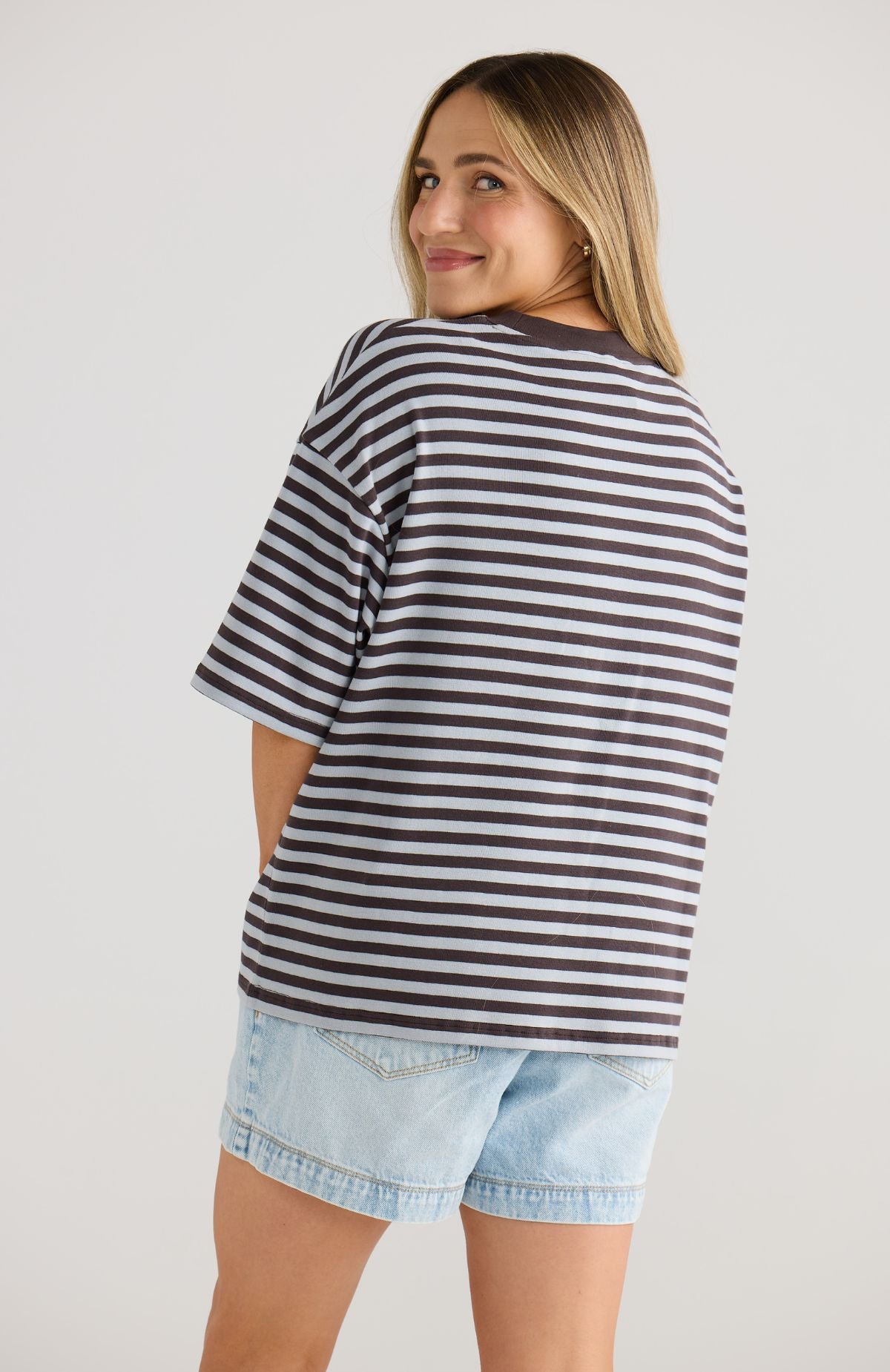 Woman wearing a striped top and denim shorts on a plain background